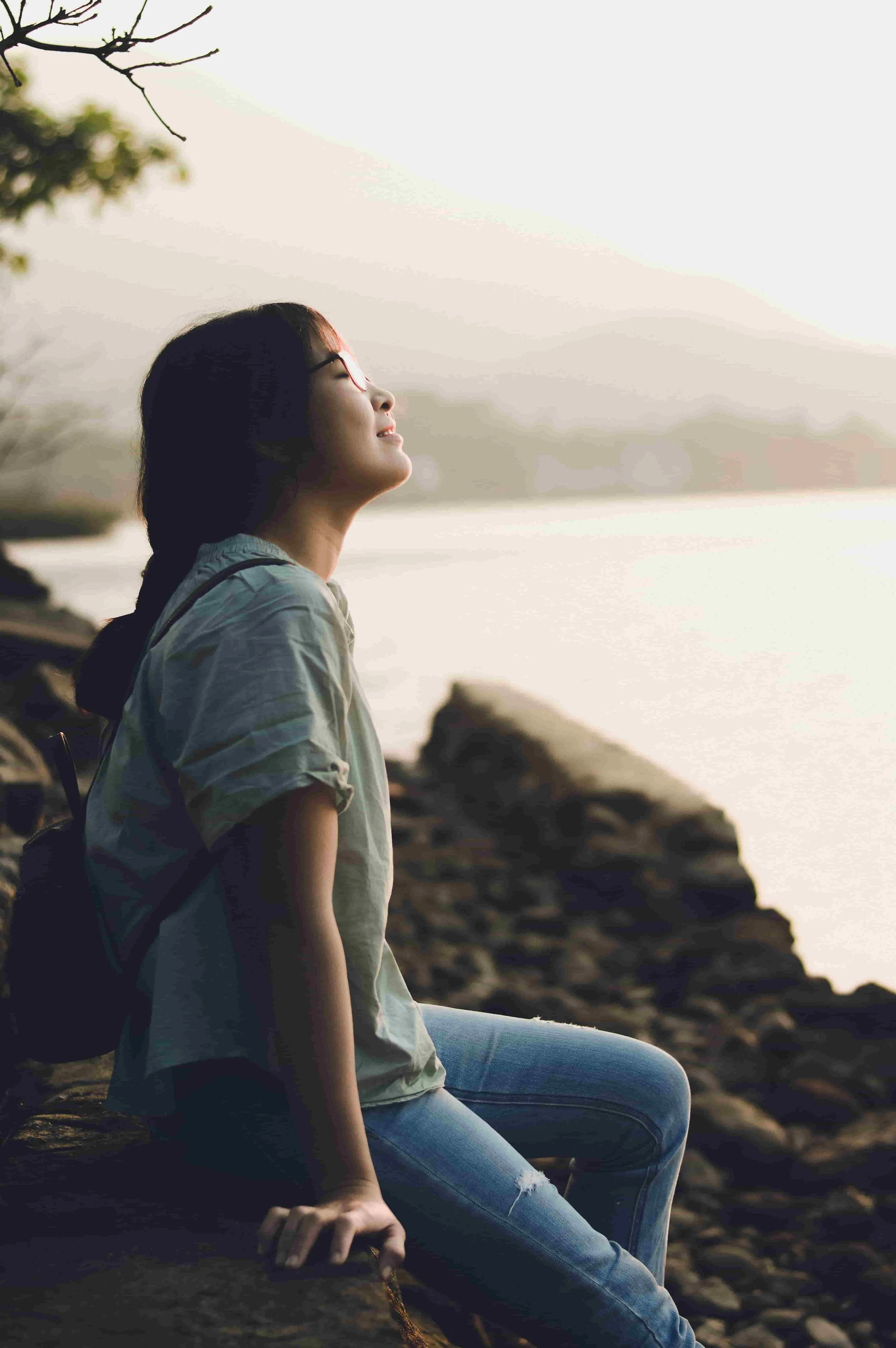 Woman sitting by the water and looking upward, representing therapy for high achievers seeking relief from burnout and pressure