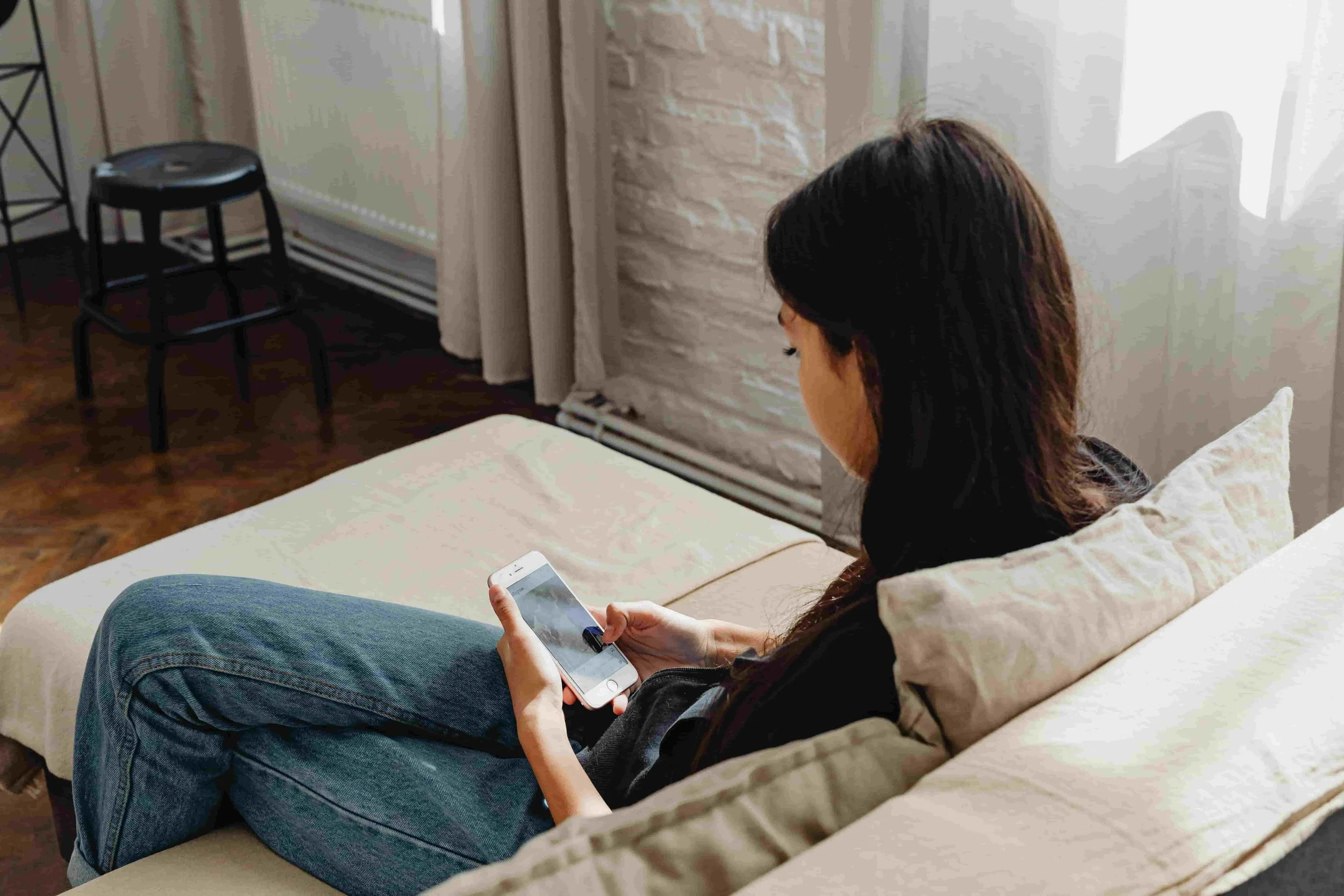 Asian American woman asking herself, "Why do I feel guilty relaxing?" while she anxiously checks her phone for emails from work.