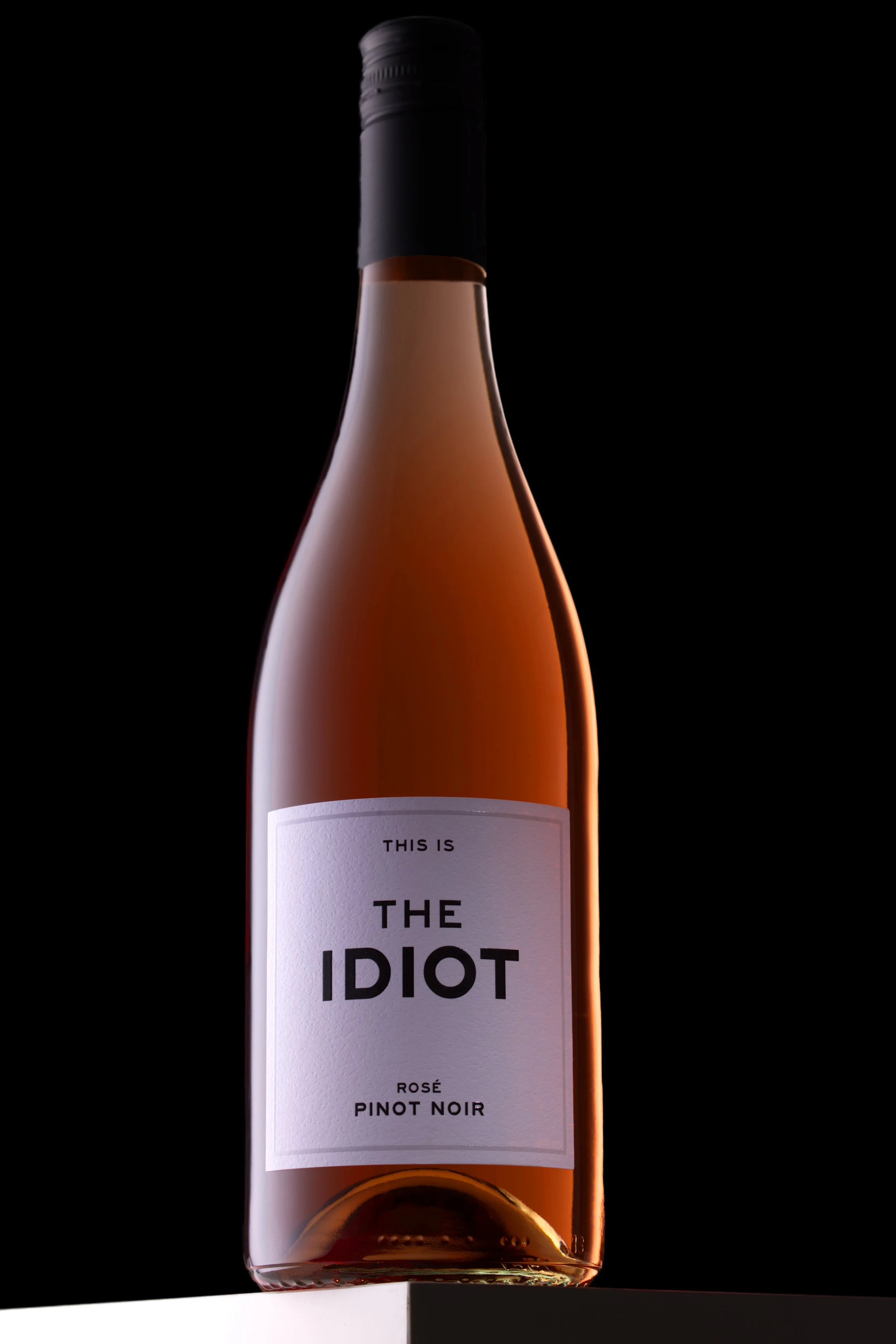 The Idiot Pinot Noir rosévin på en vit skiva med svart bakgrund. Fotograferat low key med ljus och skuggor.
