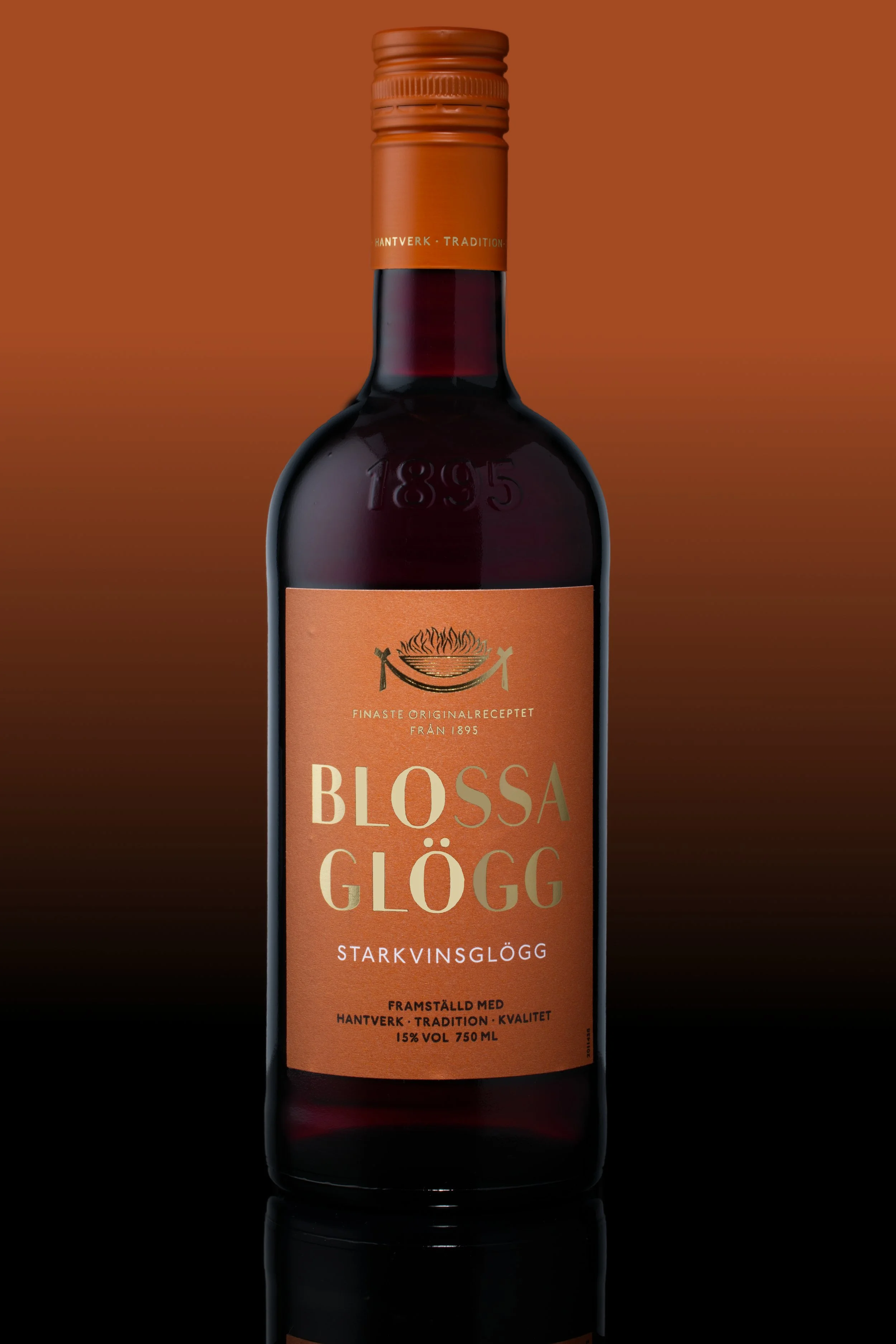 En flaska Blossa Starkvinsglögg med orange och guld etikett mot en orange bakgrund och svart glansigt underlag.