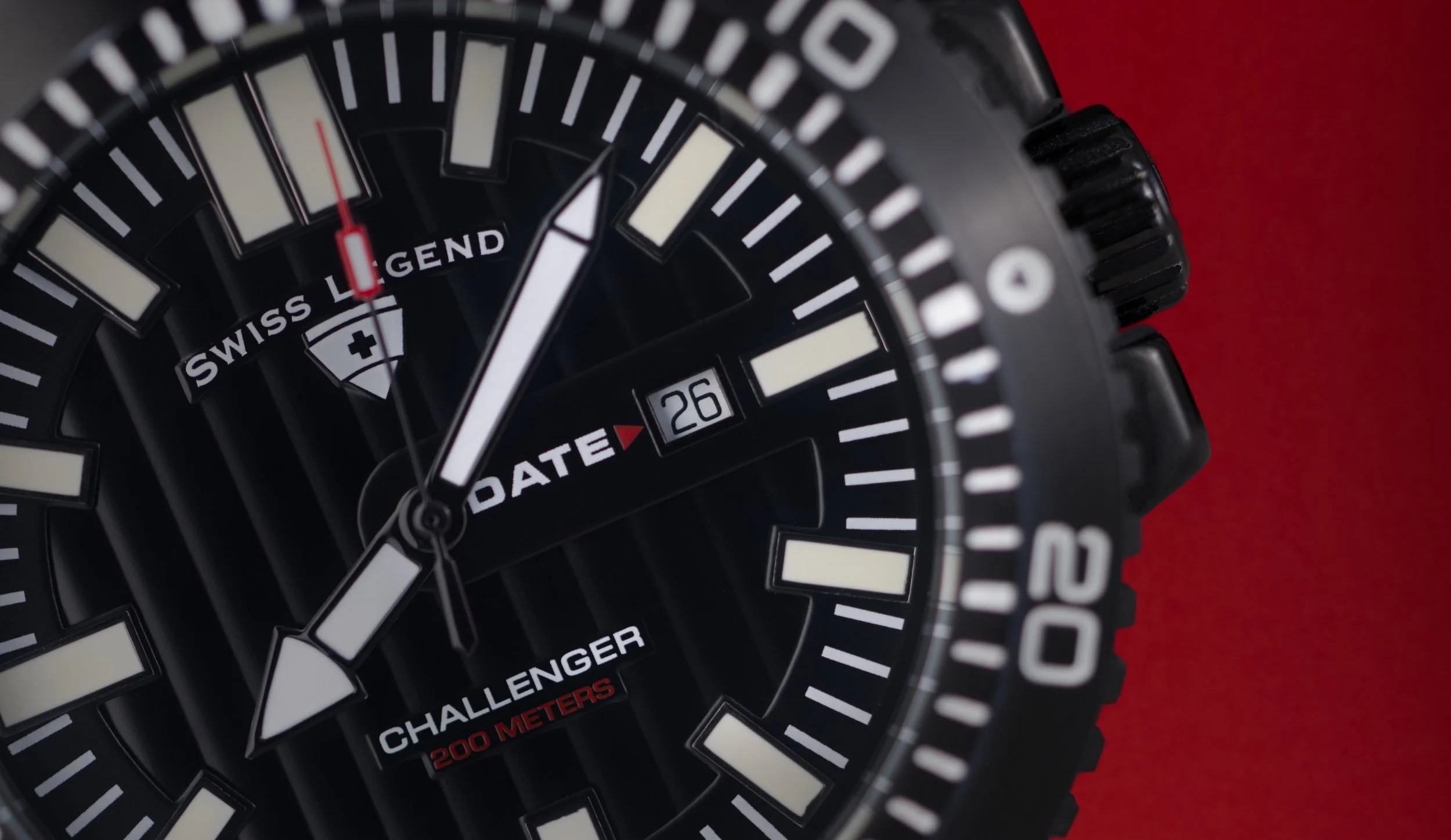 Inzoomad urtavla på klocka av märket Swiss Legend och modell Challenger i närbild med kort skärpedjup mot en röd bakgrund.