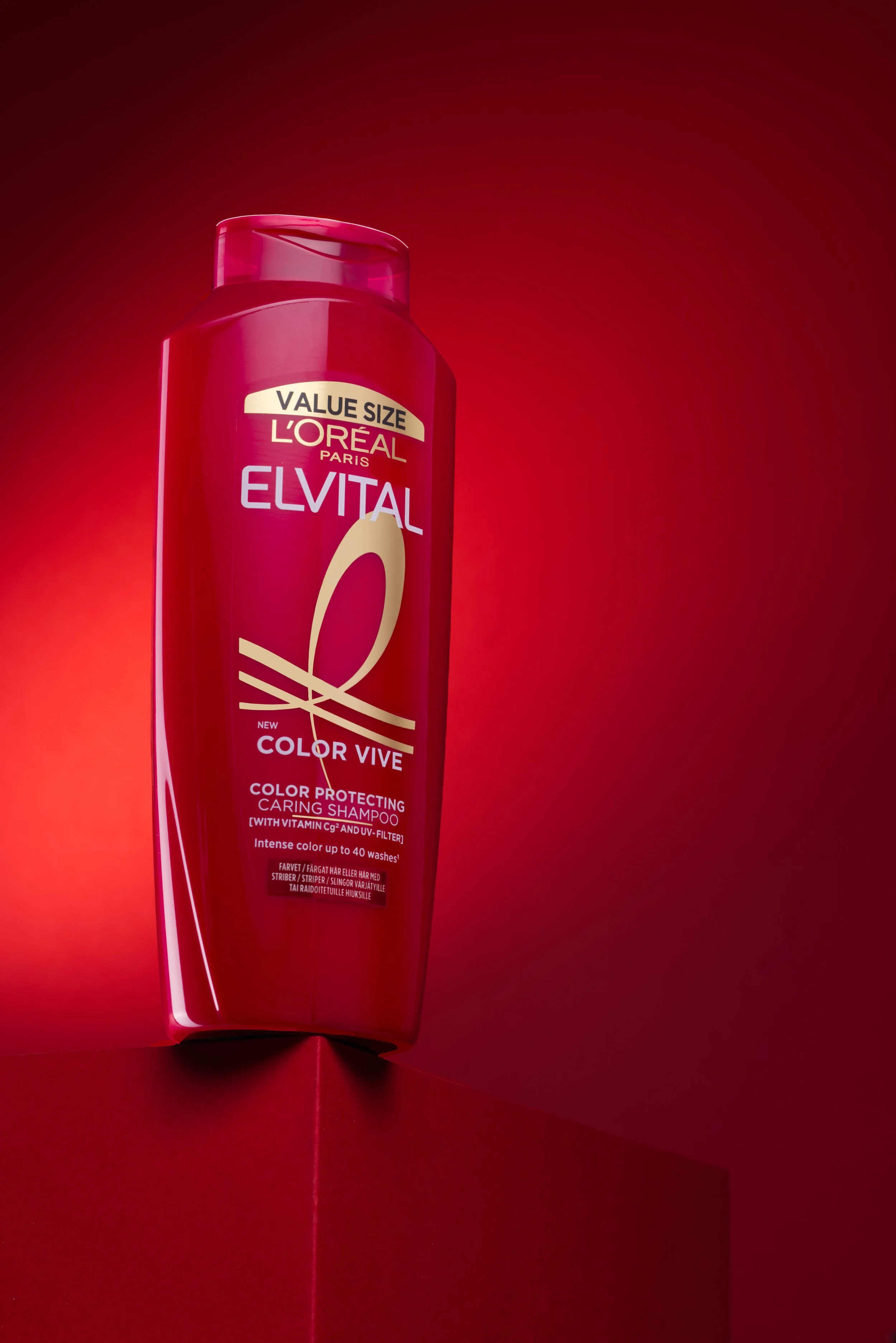 Röd L'Oreal Elvital schampoflaska på kanten av en röd piedestal fotad mot en röd delvis belyst bakgrund.