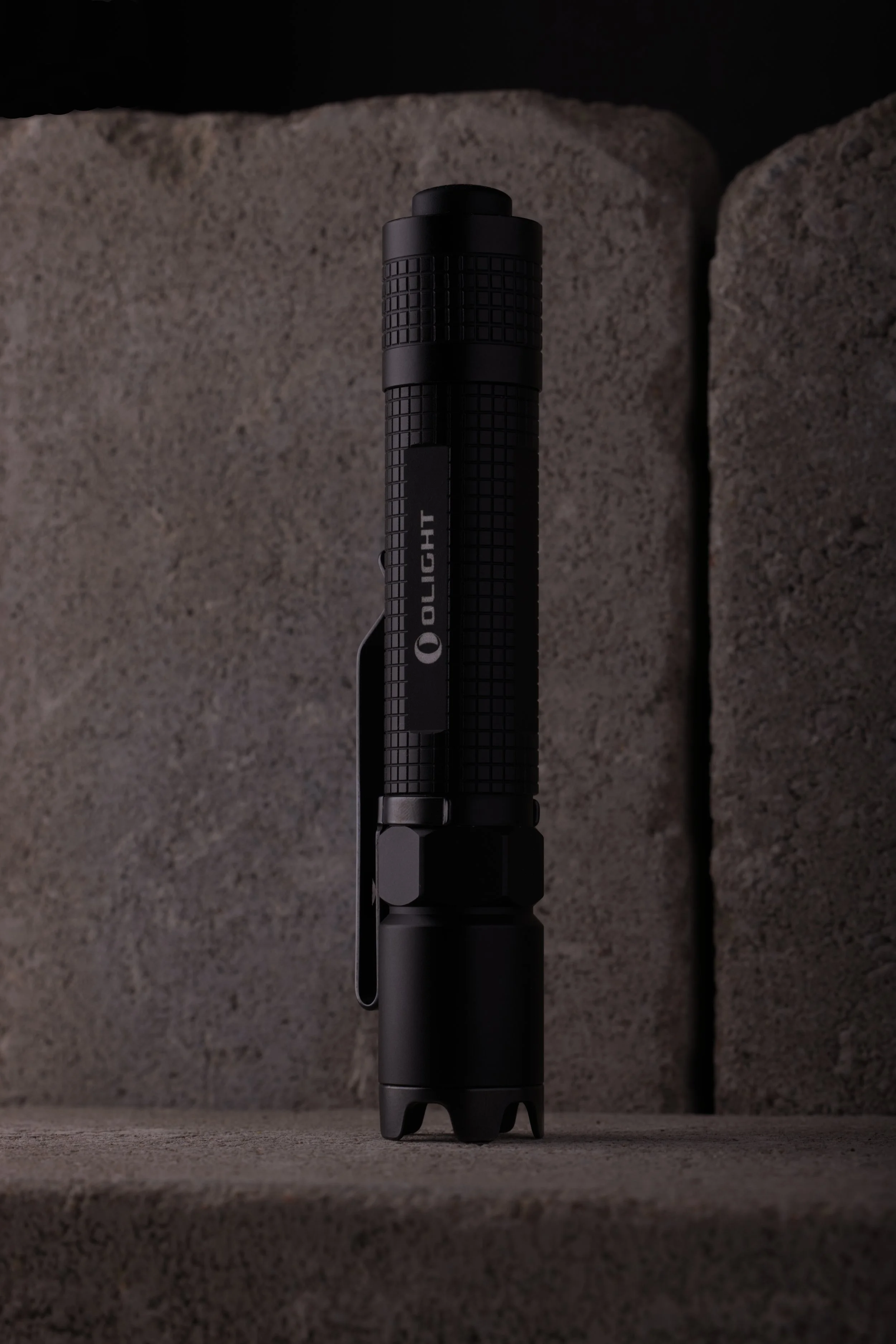 Olight M18 Striker ficklampa med grå markstenar i betong som bakgrund. Low Key.
