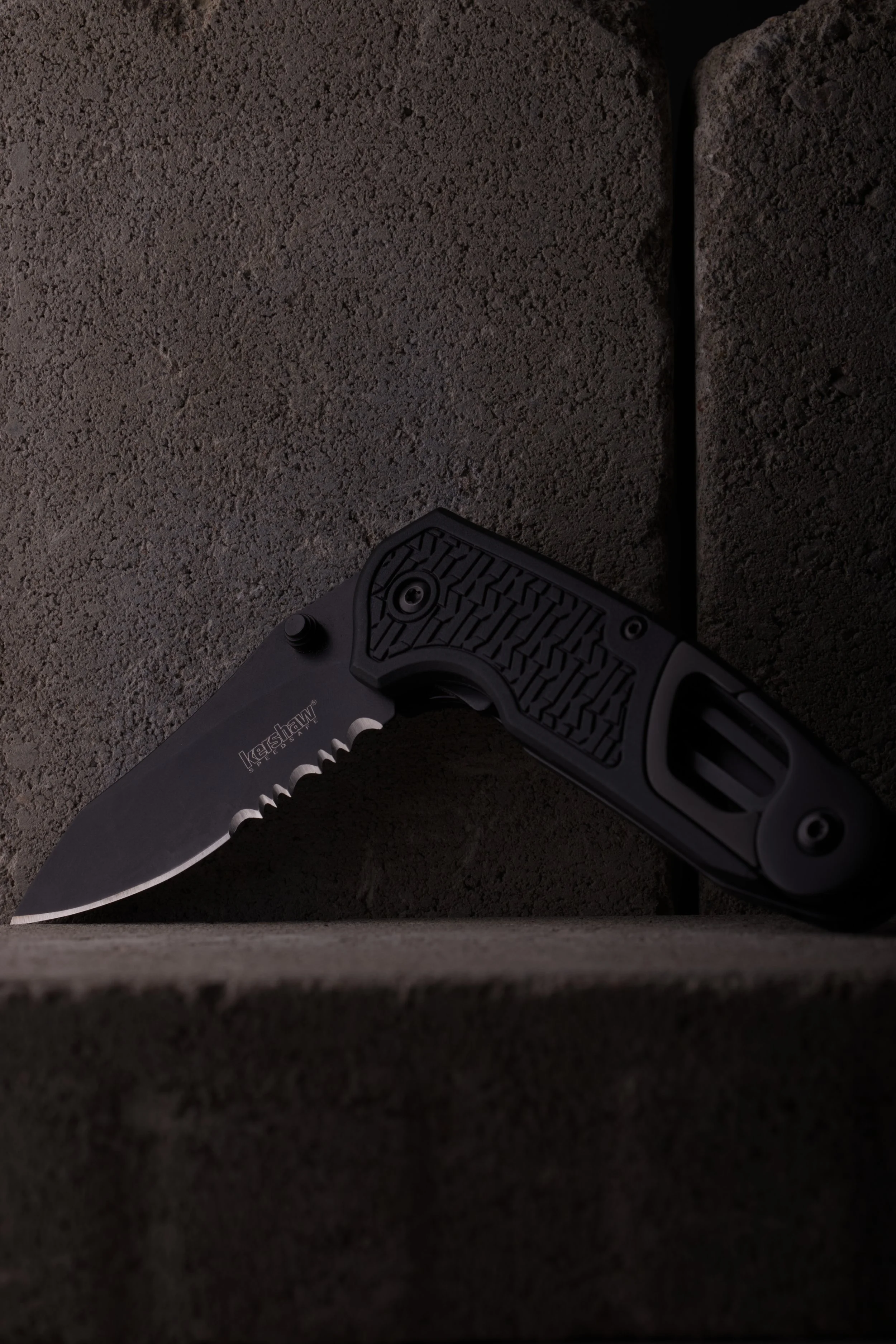 Kershaw Funxion EMT fällkniv mot en bakgrund av grå marksten i betong. Low Key.