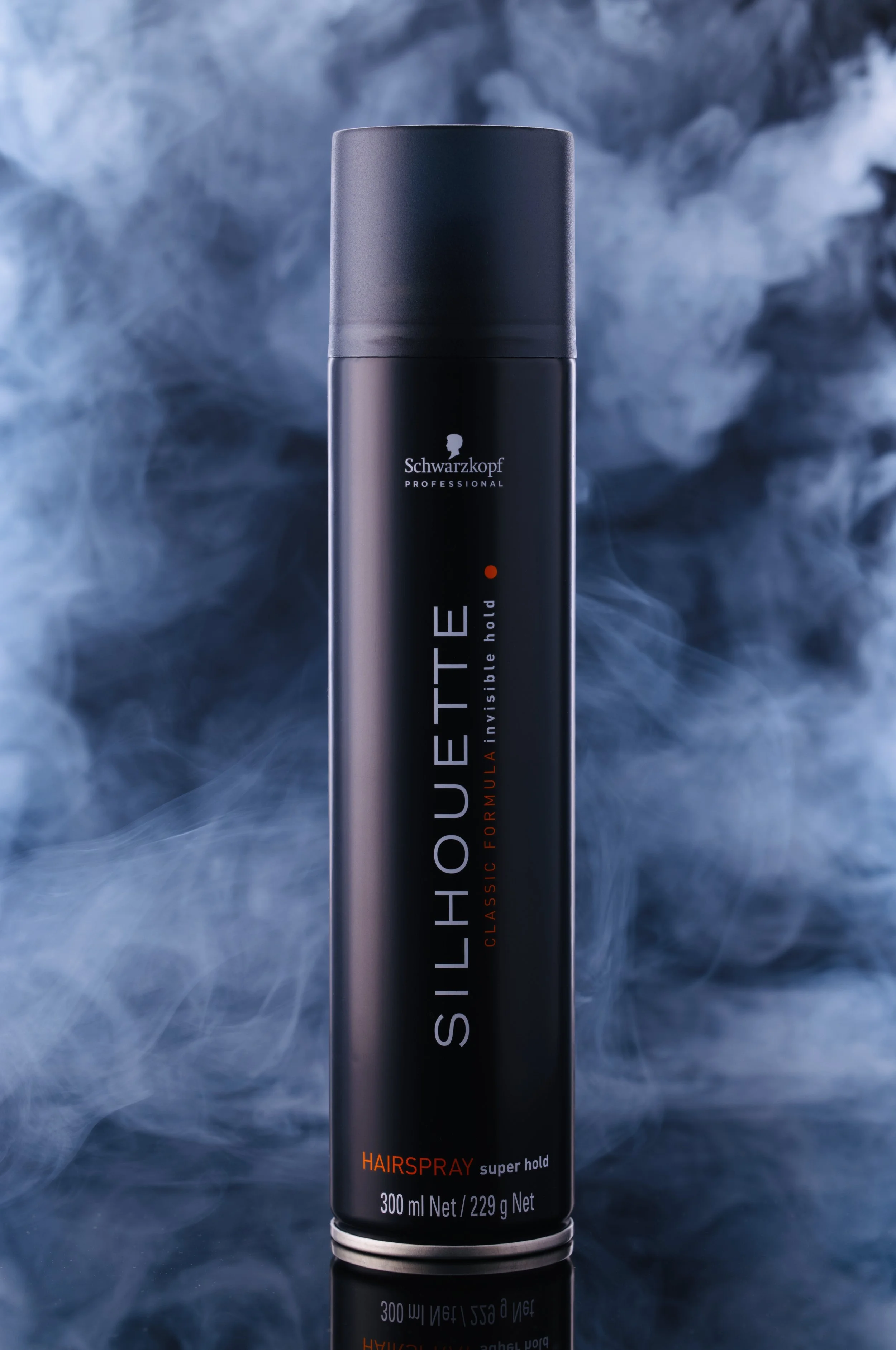 Schwarzkopf Silhouette Hairspray flaska med reflektion i svart spegelunderlag. Svart bakgrund med belyst rök.