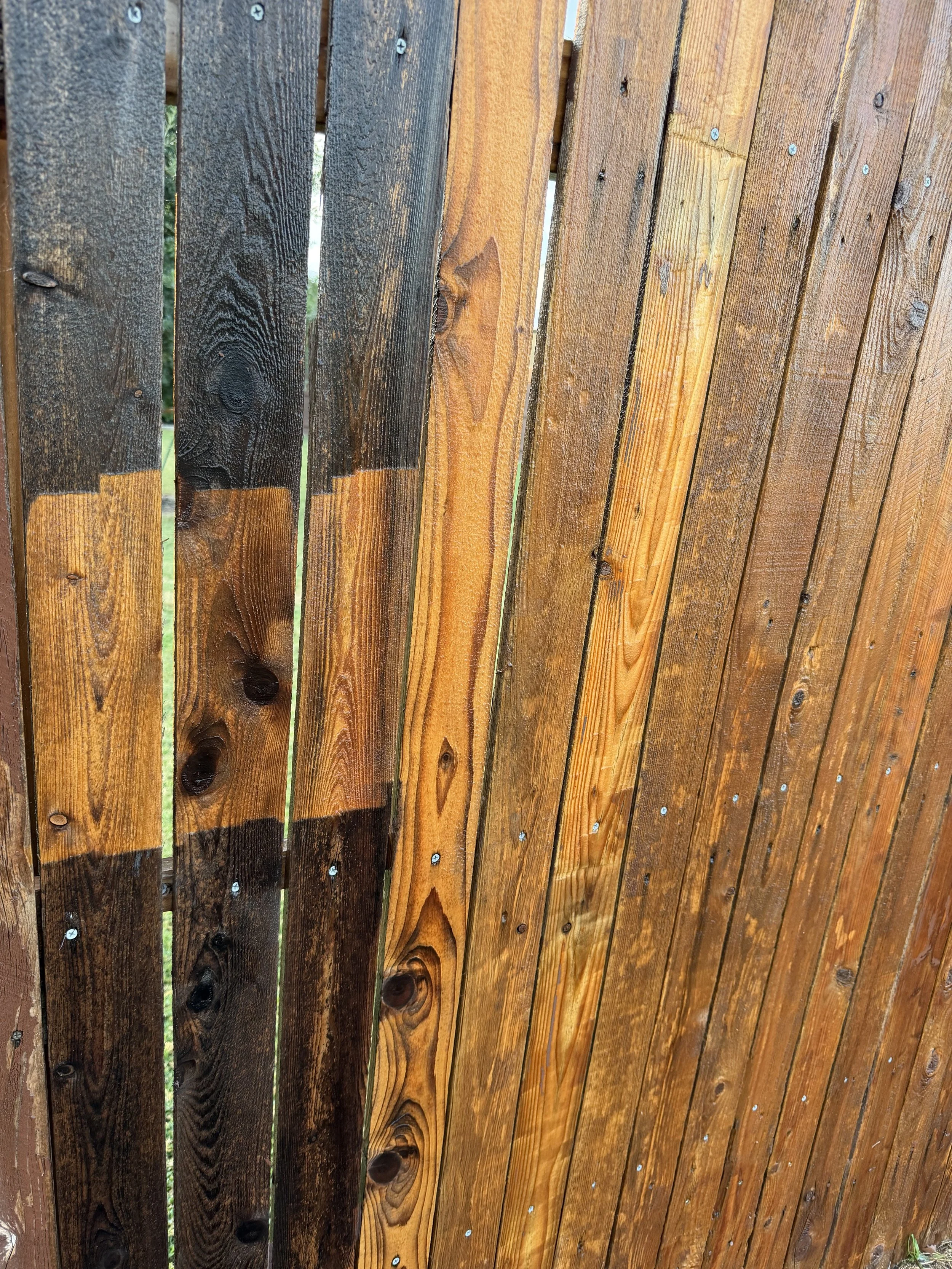 Close-up view of a wooden fence with alternating dark and light stained vertical planks, fastened with metal screws.