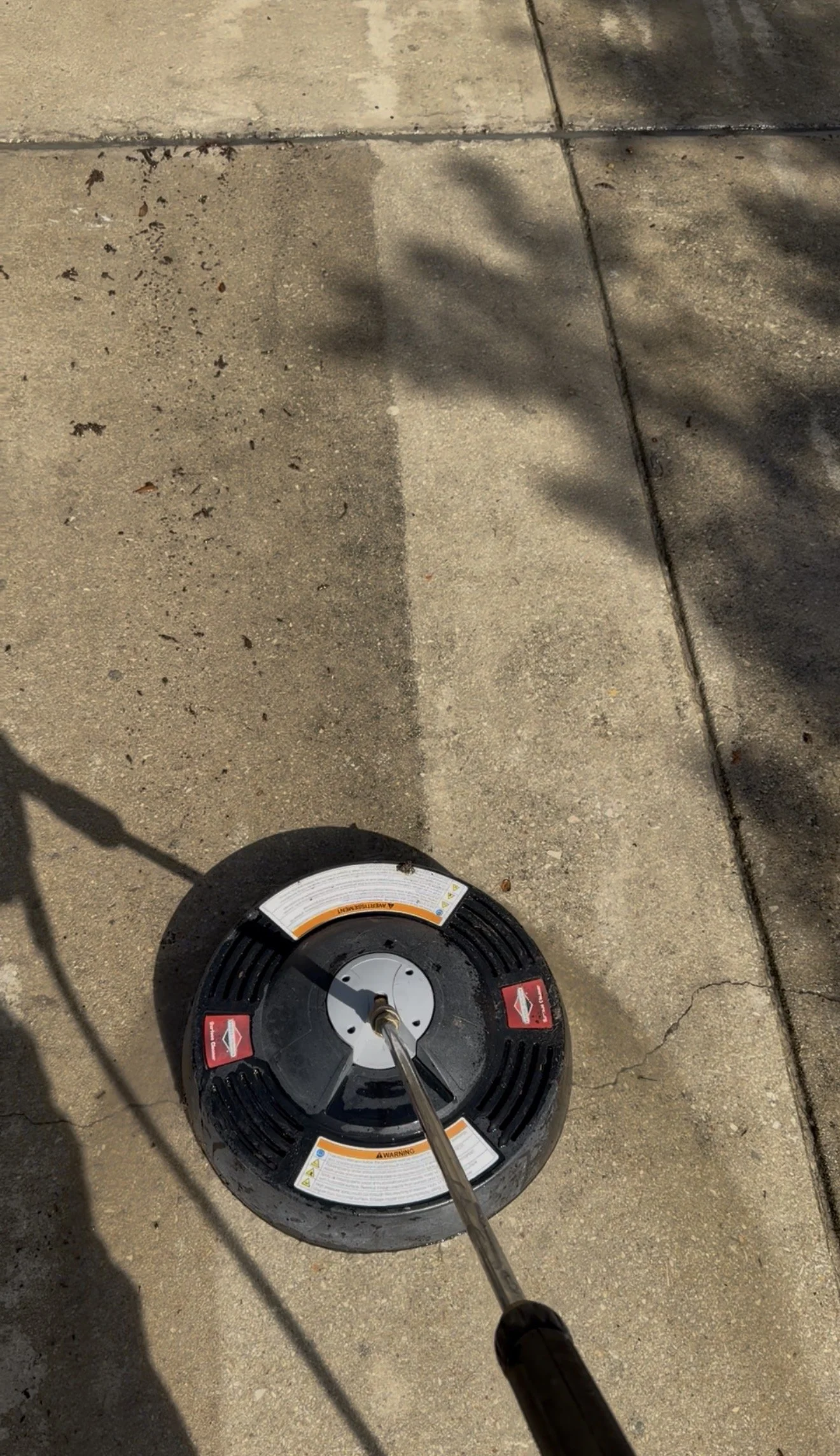 Close-up of a reel of electrical wire on the concrete ground, with the person's shadow and some shadows of nearby objects visible.