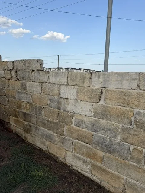 A beige brick wall with a cloudy blue sky and power lines in the background.