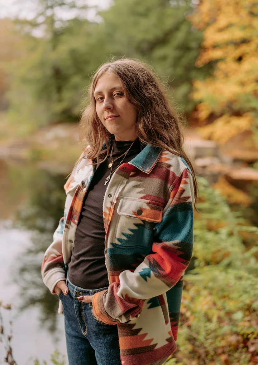 A young woman stands against an autumnal background for a portrait photo.