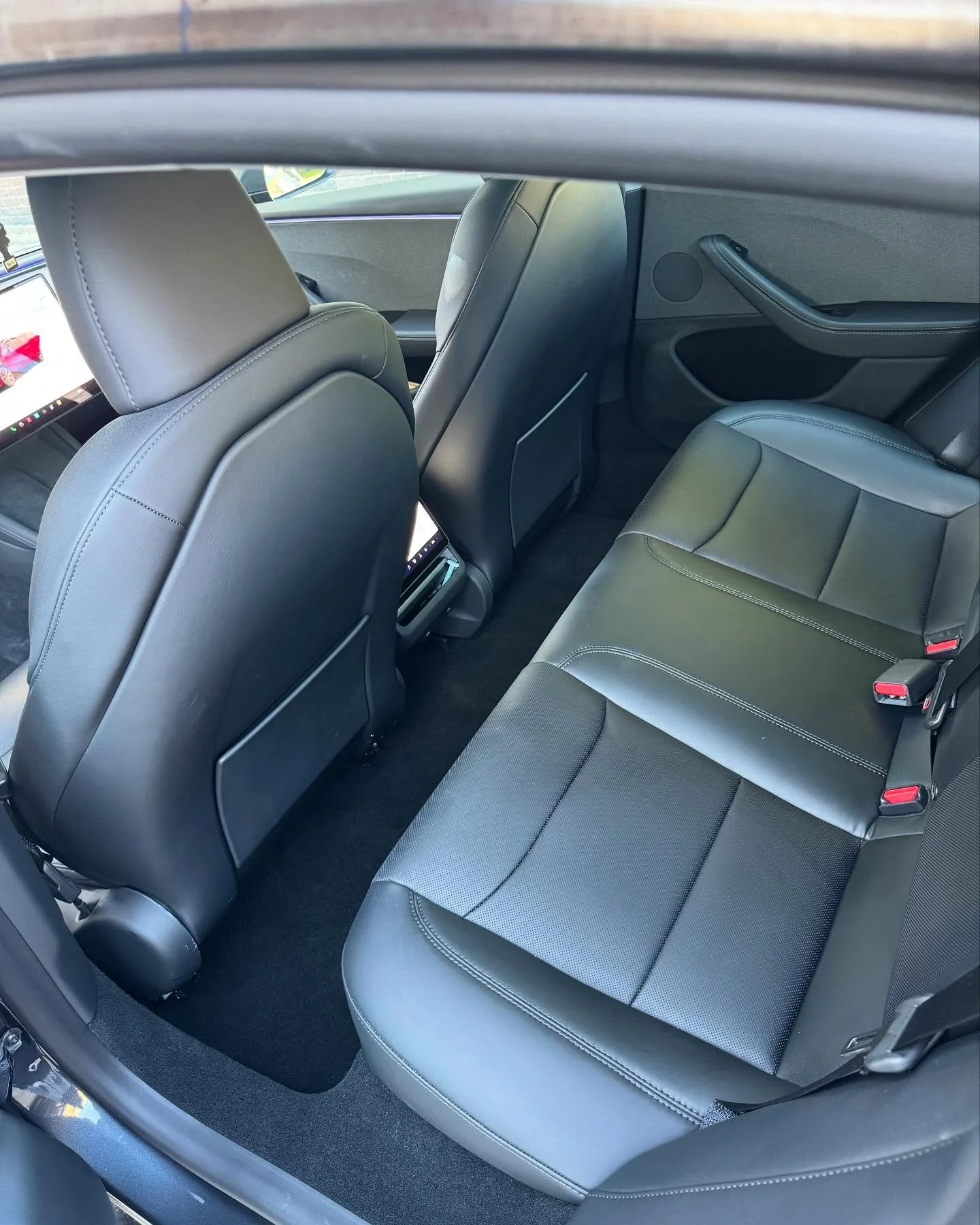 The backseat interior of a modern car with black leather seats, rear entertainment screens on the back of the front seats, and black carpeting.