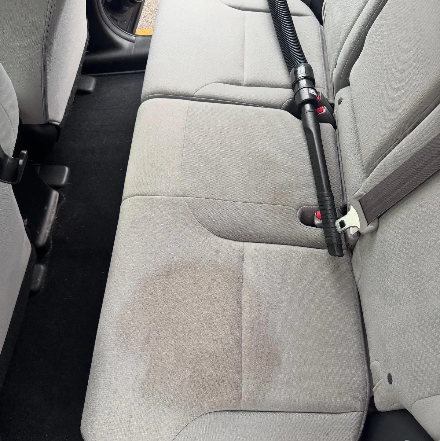 The backseat of a vehicle with a portable vacuum cleaner placed across it.
