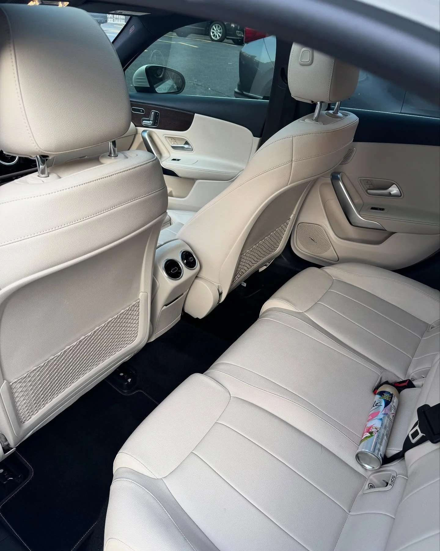 The interior of a beige leather car showing the back seat, front seats, and air conditioning vents, with a water bottle on the back seat.