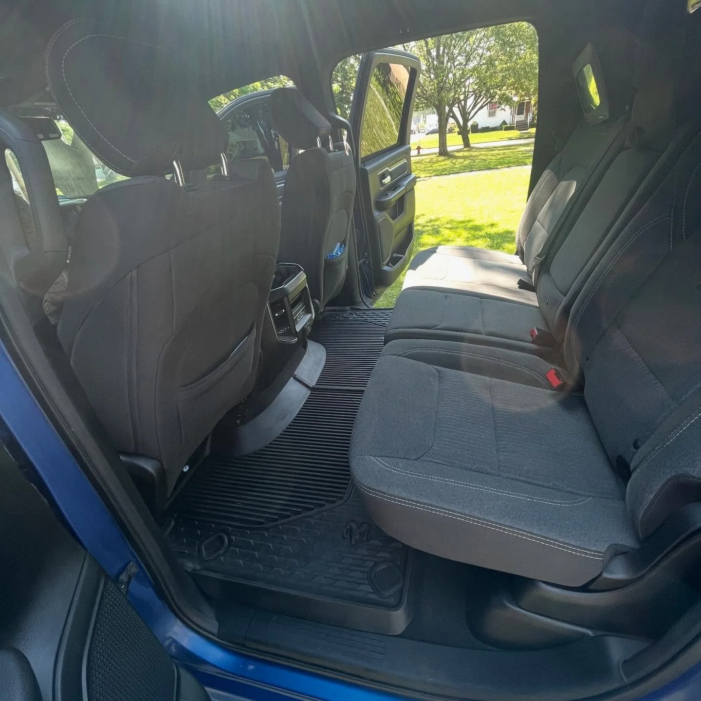 Interior of a blue pickup truck with rear bench seat, black seats, and open door showing a grassy yard with trees outside.