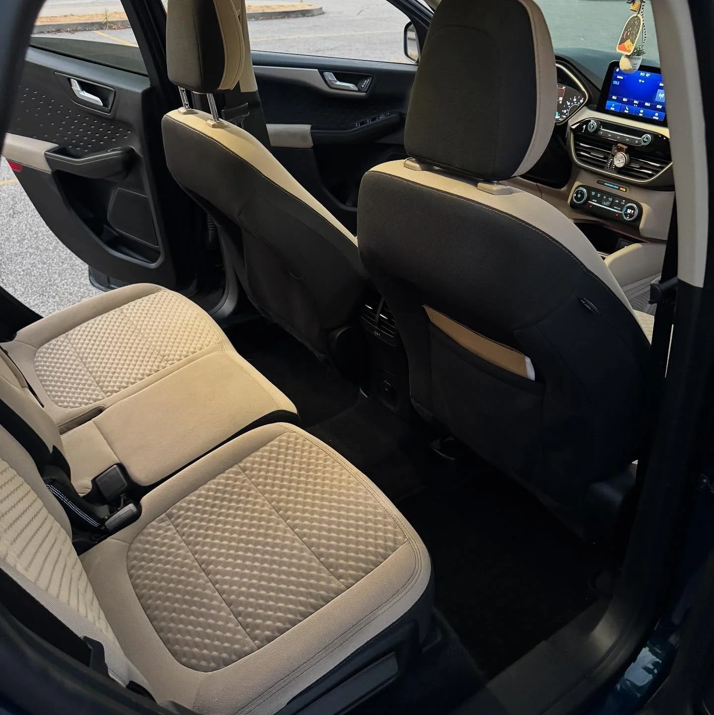 Interior of a modern vehicle showing the back seats, the front seats, and the dashboard with a digital display.