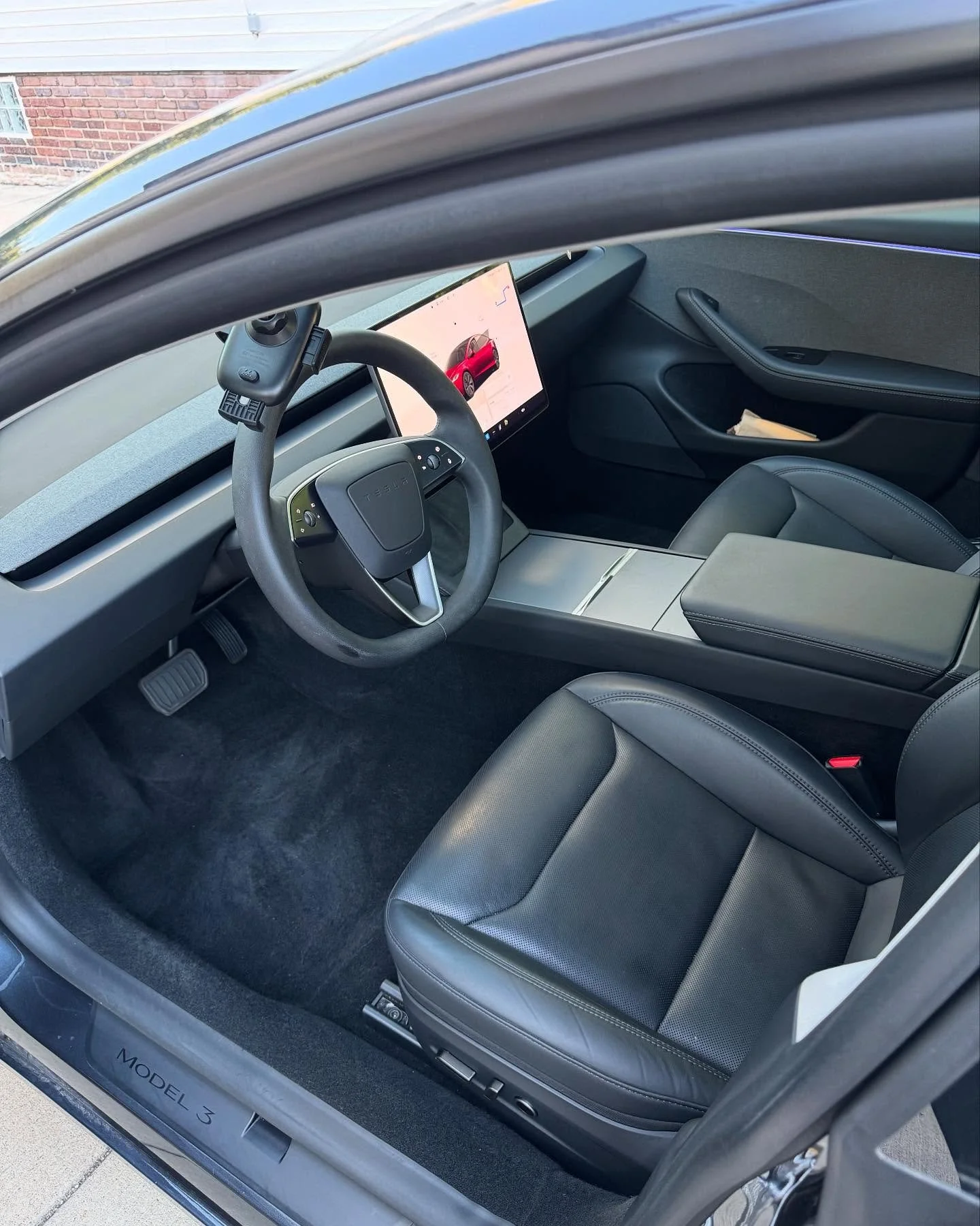 Interior of a modern electric car with a large touchscreen display, steering wheel, black leather seat, and minimalist dashboard design.