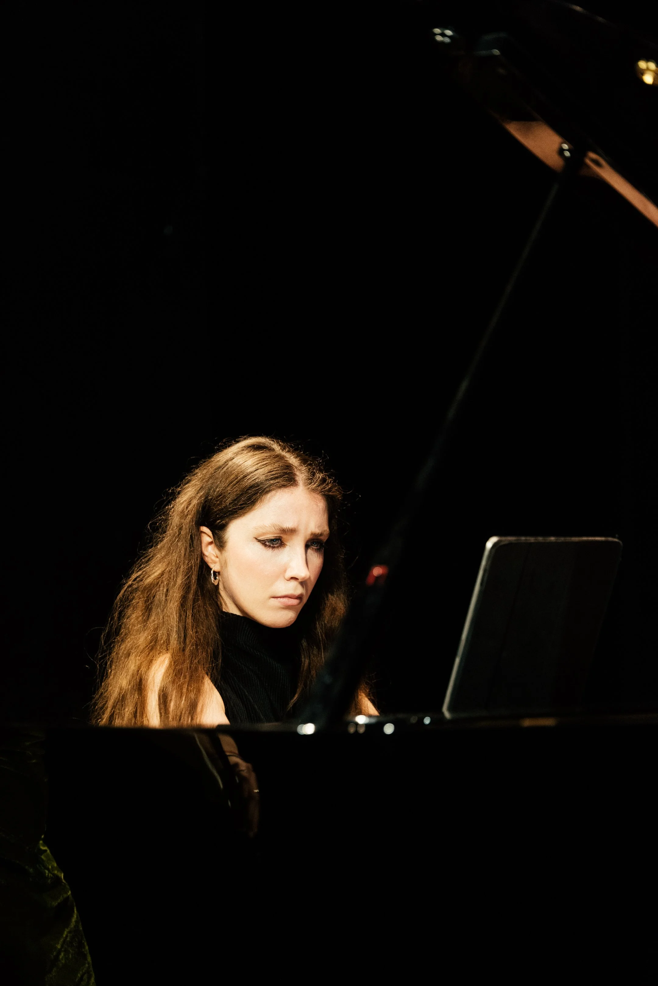 Donna giovane con capelli riccioli castani chiari su un pianoforte nero, con espressione concentrata.
