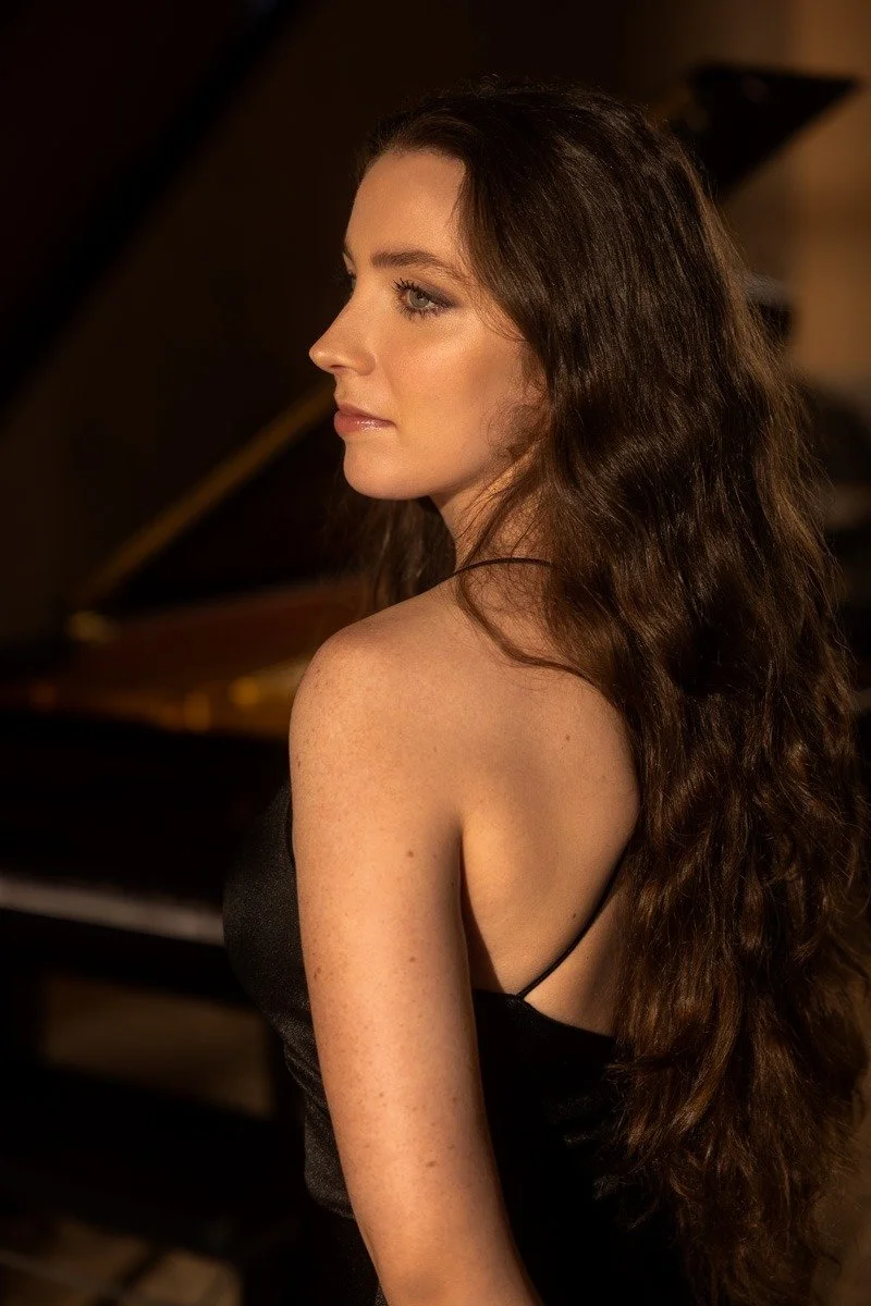 Ragazza con capelli lunghi e ricci seduta davanti a un pianoforte, vista laterale del volto e spalle