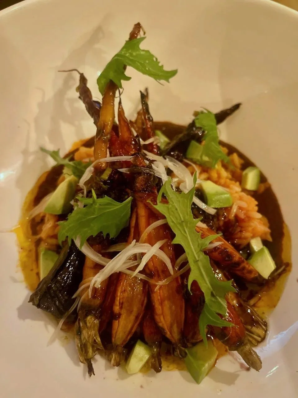 Front view of a plate of grilled shrimp garnished with fresh greens and sliced vegetables.