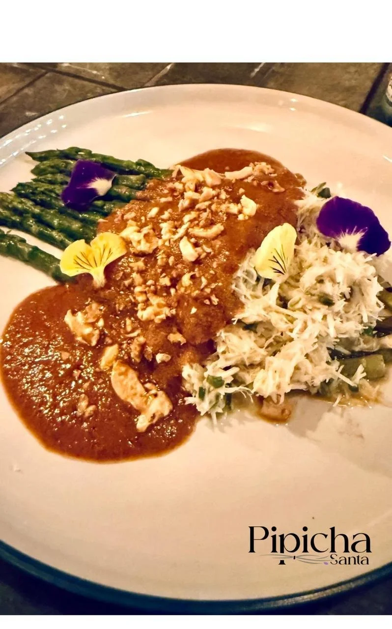 Plate with asparagus spears, shredded chicken salad, and a main dish with sauce topped with chopped nuts, garnished with edible flowers from Pipicha restaurant in Santa.