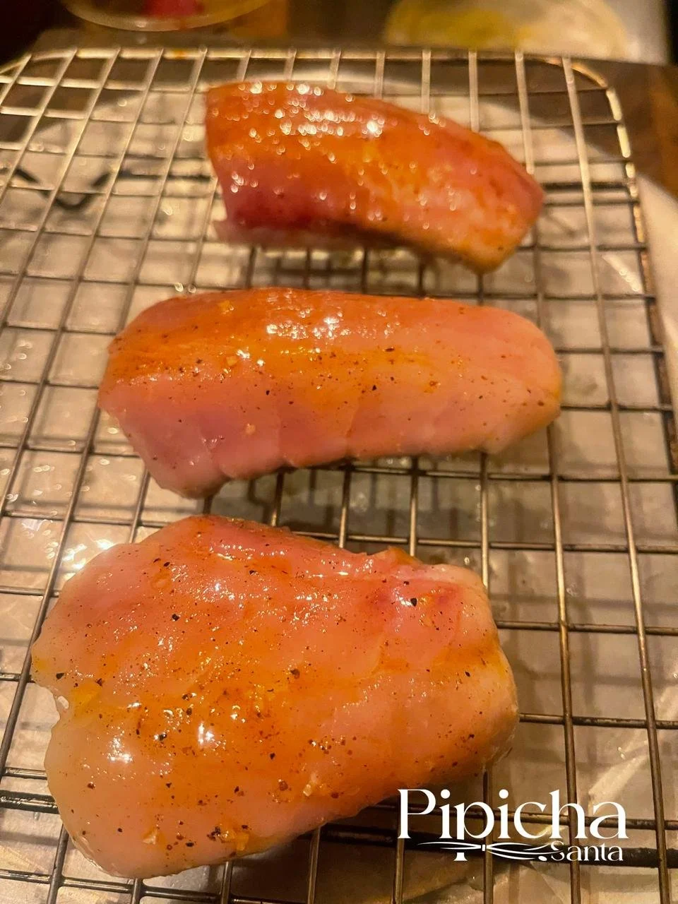 Three seasoned raw chicken breasts on a wire rack.