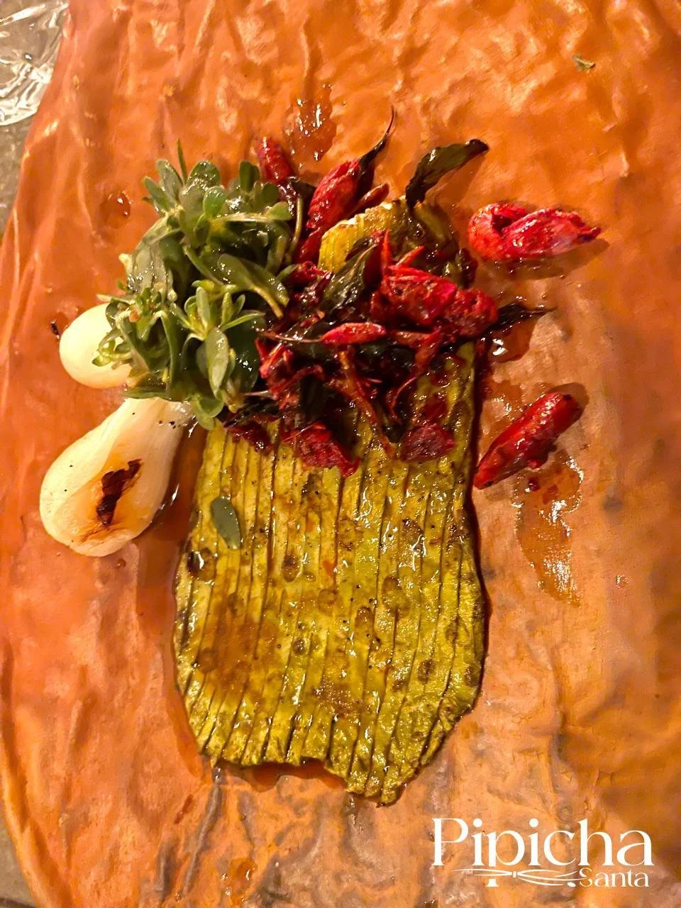 Grilled fish fillet on a wooden serving board with roasted tomatoes and herbs, served with a side of onion and a small green salad.