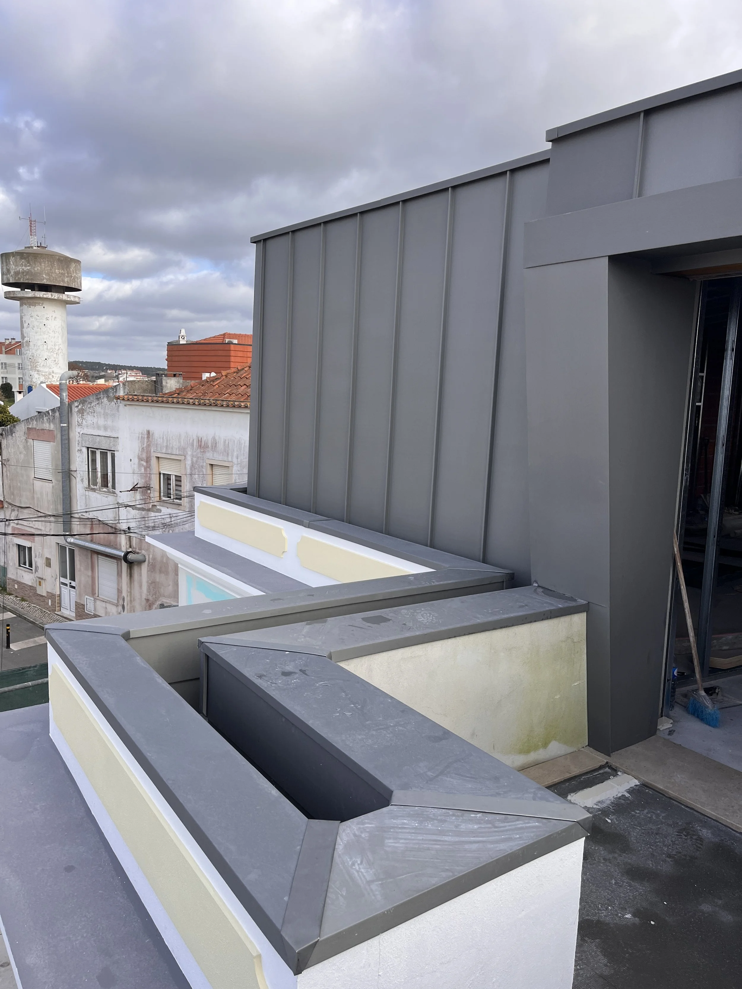 Imagem de um telhado de edifício com detalhes de paredes de metal cinza escuro, suportes de plantas sem plantas, sob céu parcialmente nublado.