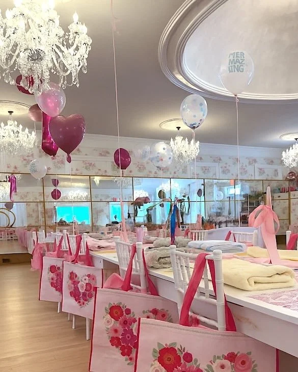 Party setup at The Madison Soirée in Madison, NJ, with crystal chandeliers, pink balloons, and floral tote bags on white chairs.