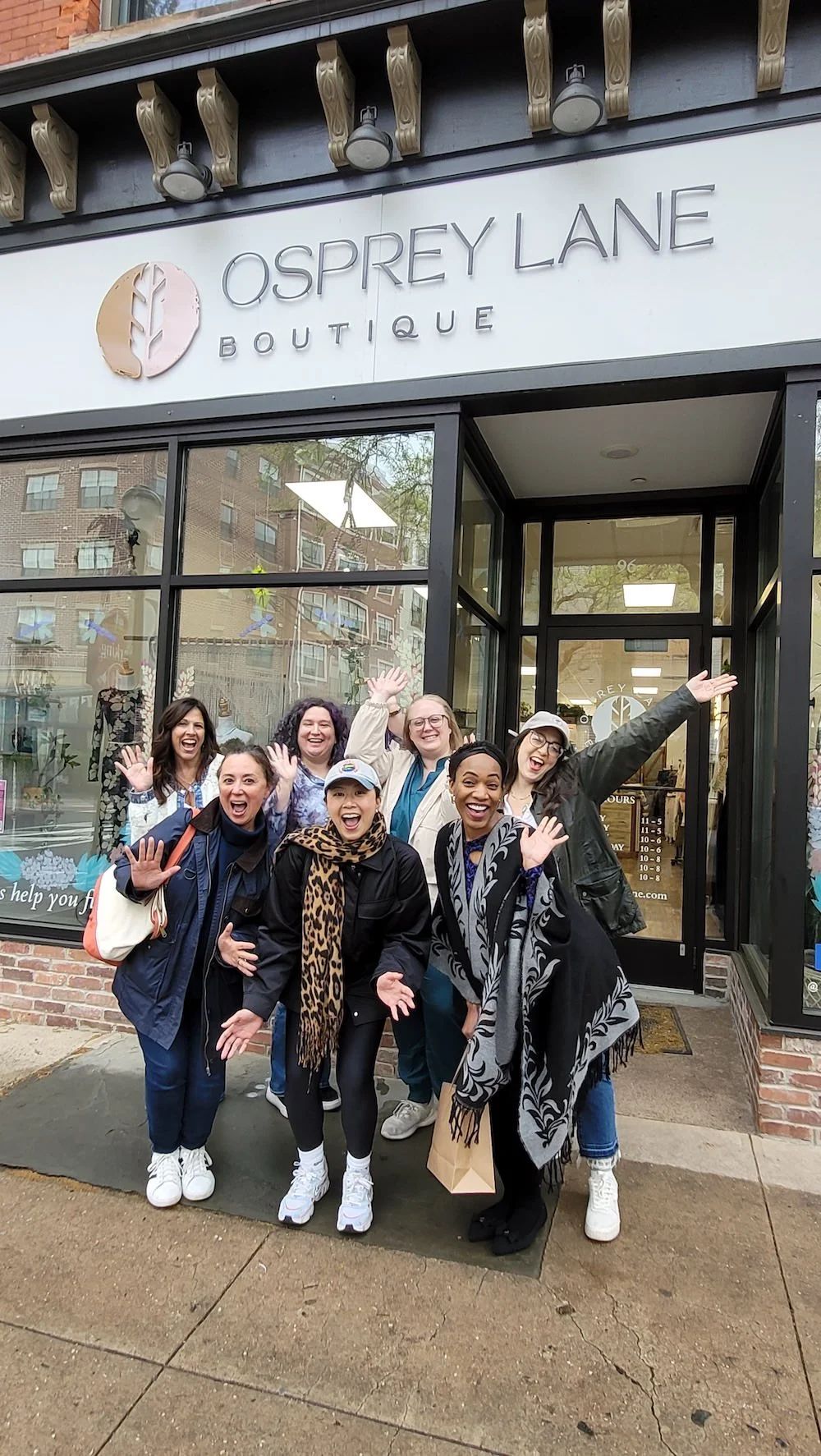 A group of smiling women in Somerville, NJ standing outside a boutique named Osprey Lane, waving at the camera.