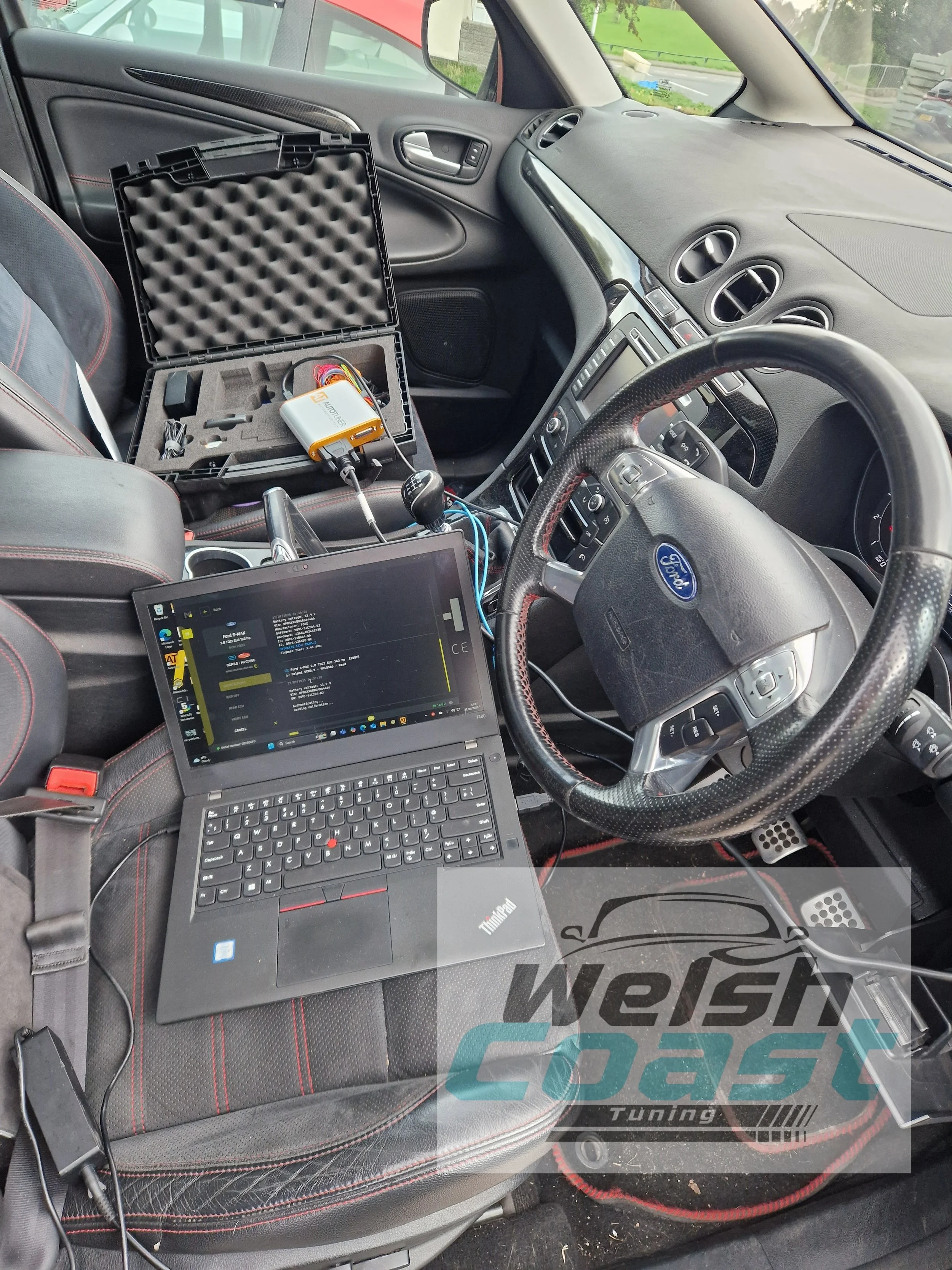 Inside a vehicle, a laptop, a diagnostic tool, and various electronic devices are set up, indicating tuning or diagnostic work being performed.
