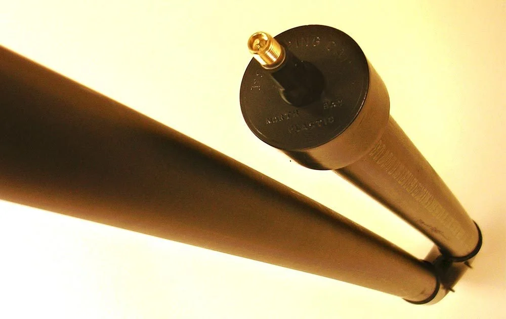 Close-up of two black cylindrical objects, mounted parallel, with a gold connector on top of one object, against a white background.