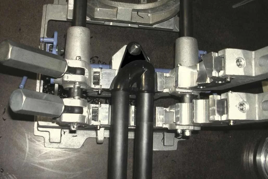 Close-up of a mechanical device with two black pipes, metal levers, and components mounted on a metal frame.
