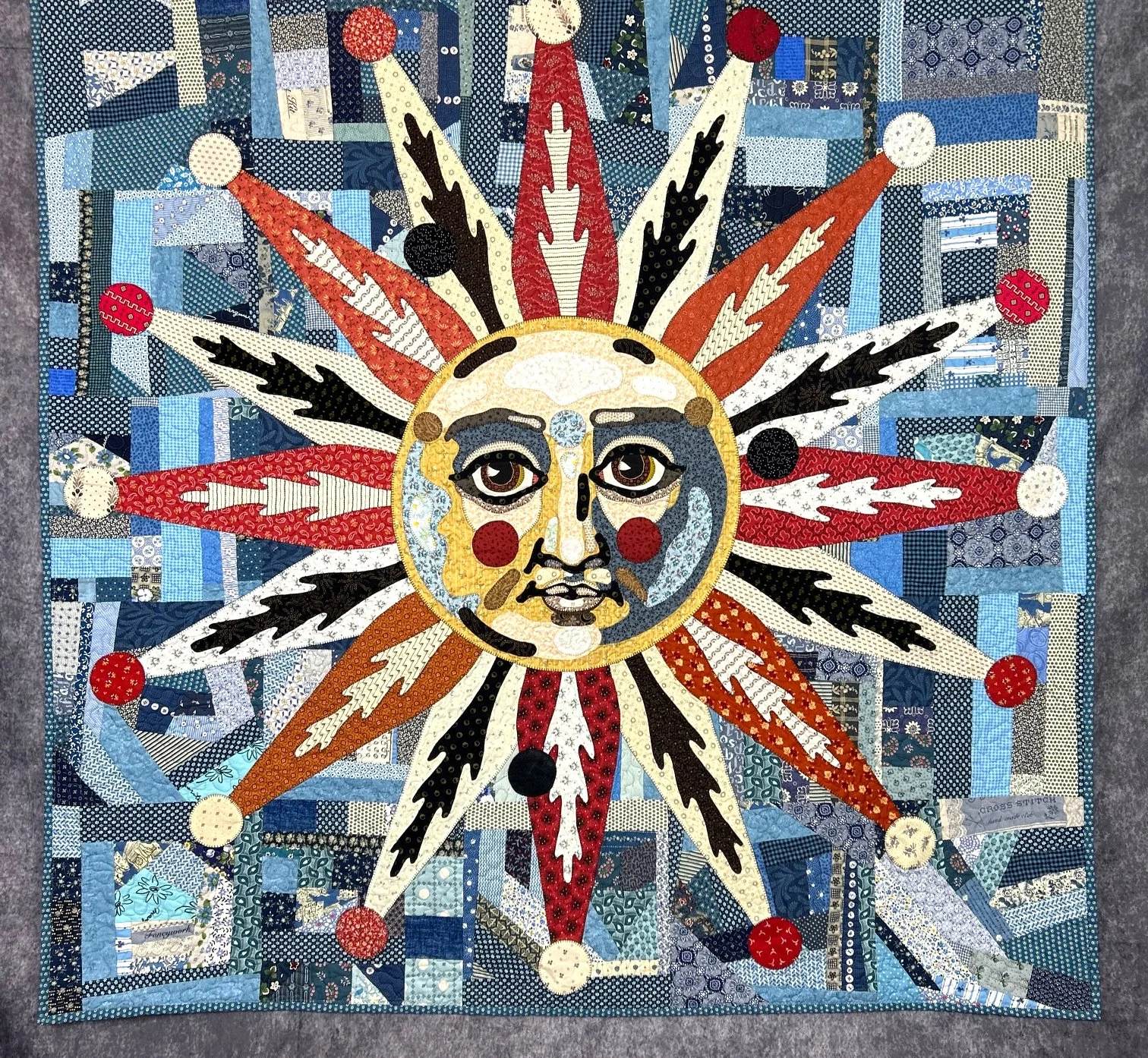 folk art quilted wall hanging of a medieval sun with red and black quilted rays