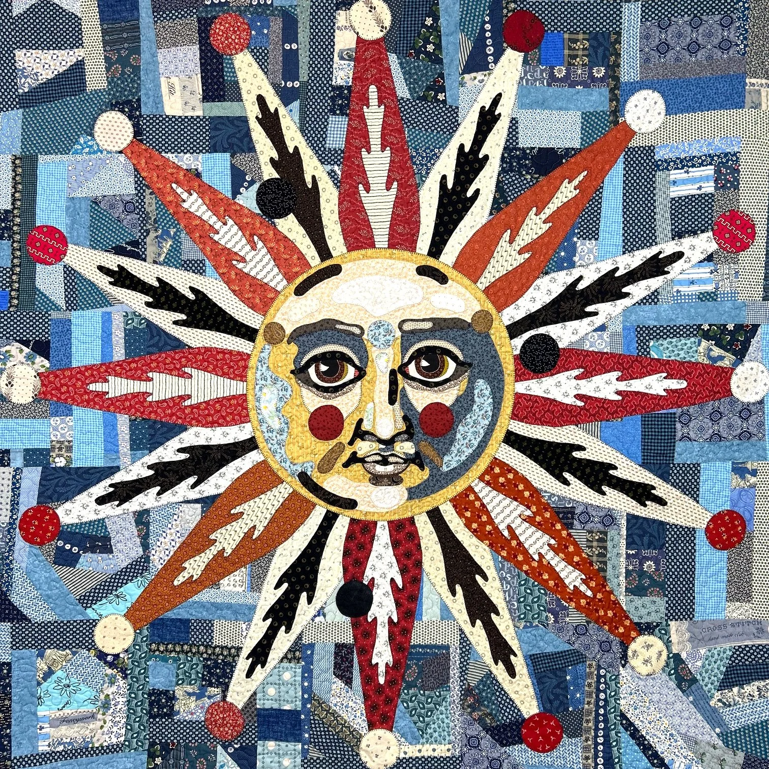 quilted wallhanging featuring an appliqued sun with red and black rays