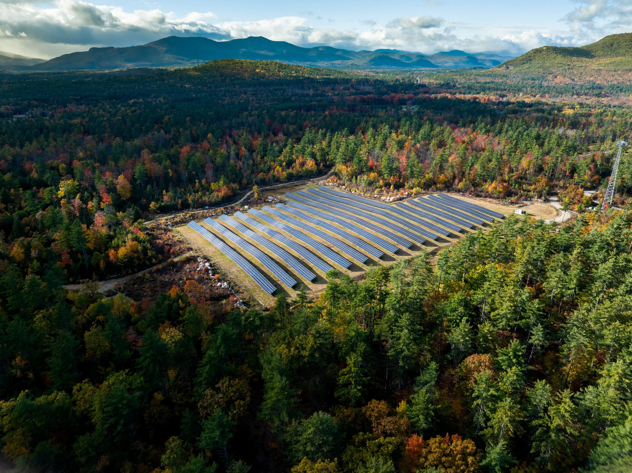 A solar panel farm located in a forested mountainous area during daytime.
