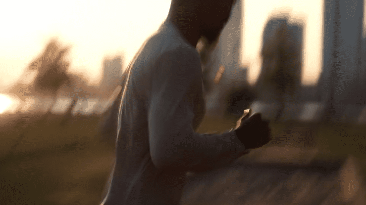 Person in a white hoodie using a smartphone outdoors during sunset or dusk.
