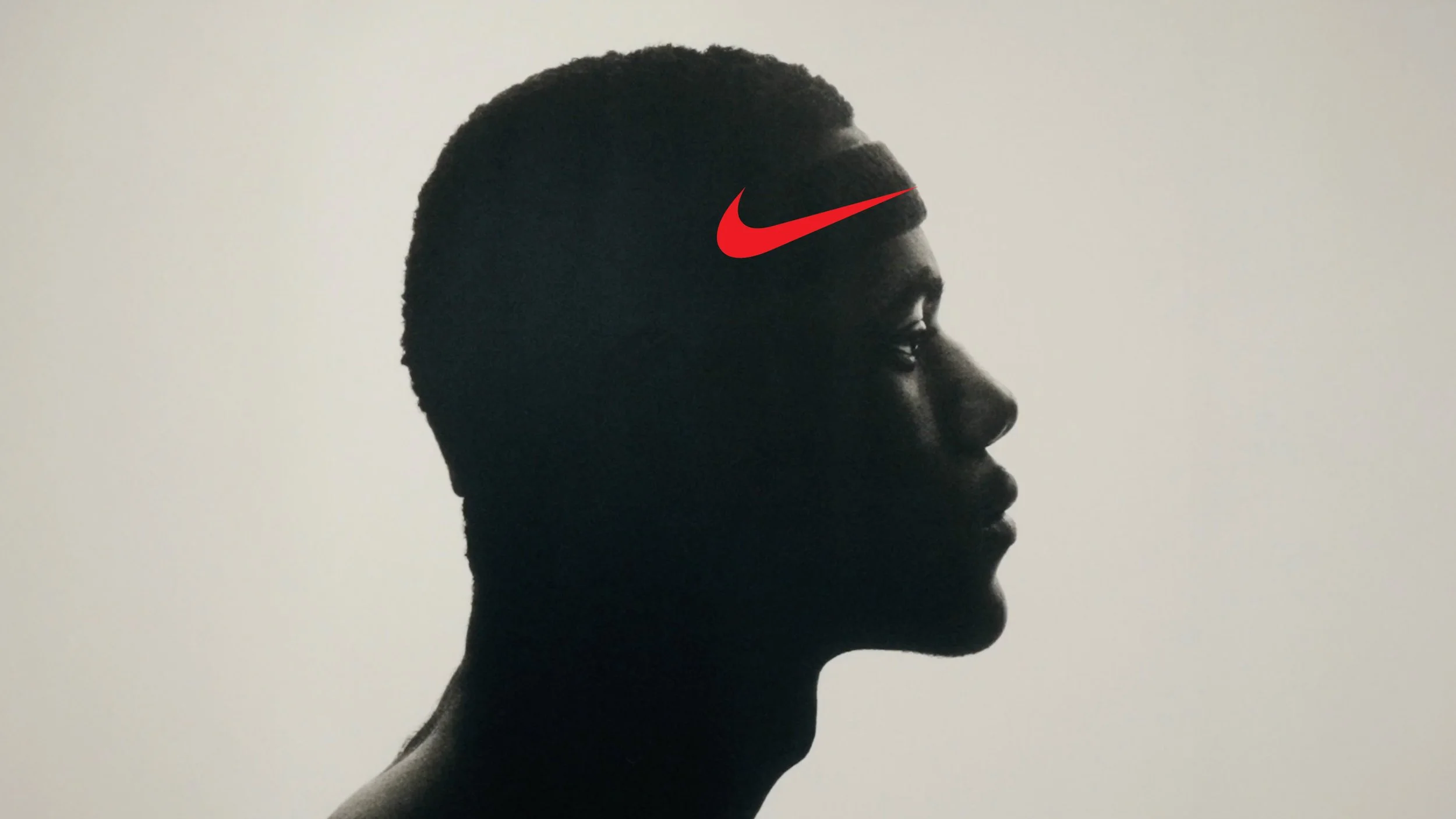Profile silhouette of a man with short hair and strong jawline facing right, with a red Nike swoosh logo on his forehead, against a plain light background.