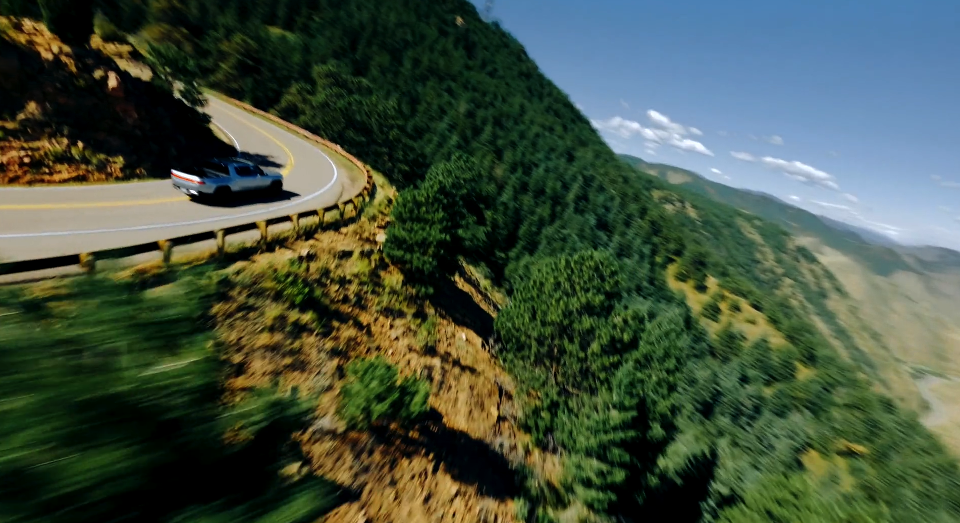 A white car driving on a winding mountain road with lush green hills and blue sky in the background.