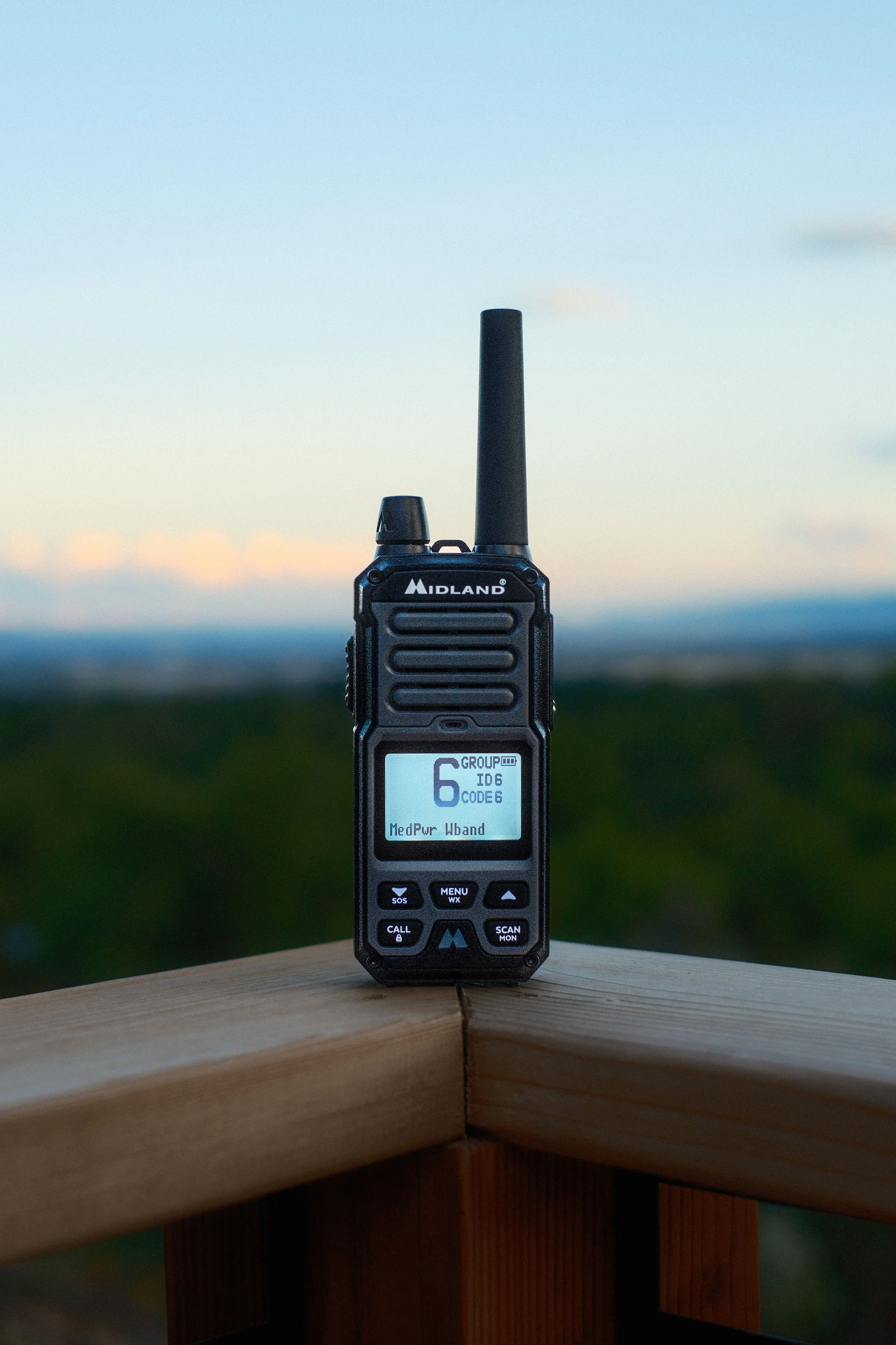 A walkie-talkie radio is placed on a wooden surface with a blurred outdoor landscape in the background.