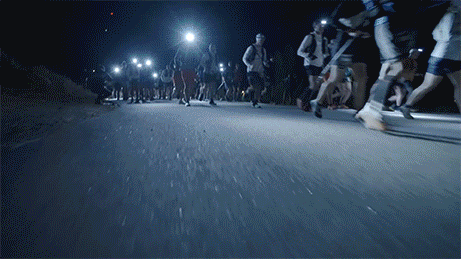 Group of people running on a dark road at night with streetlights overhead.