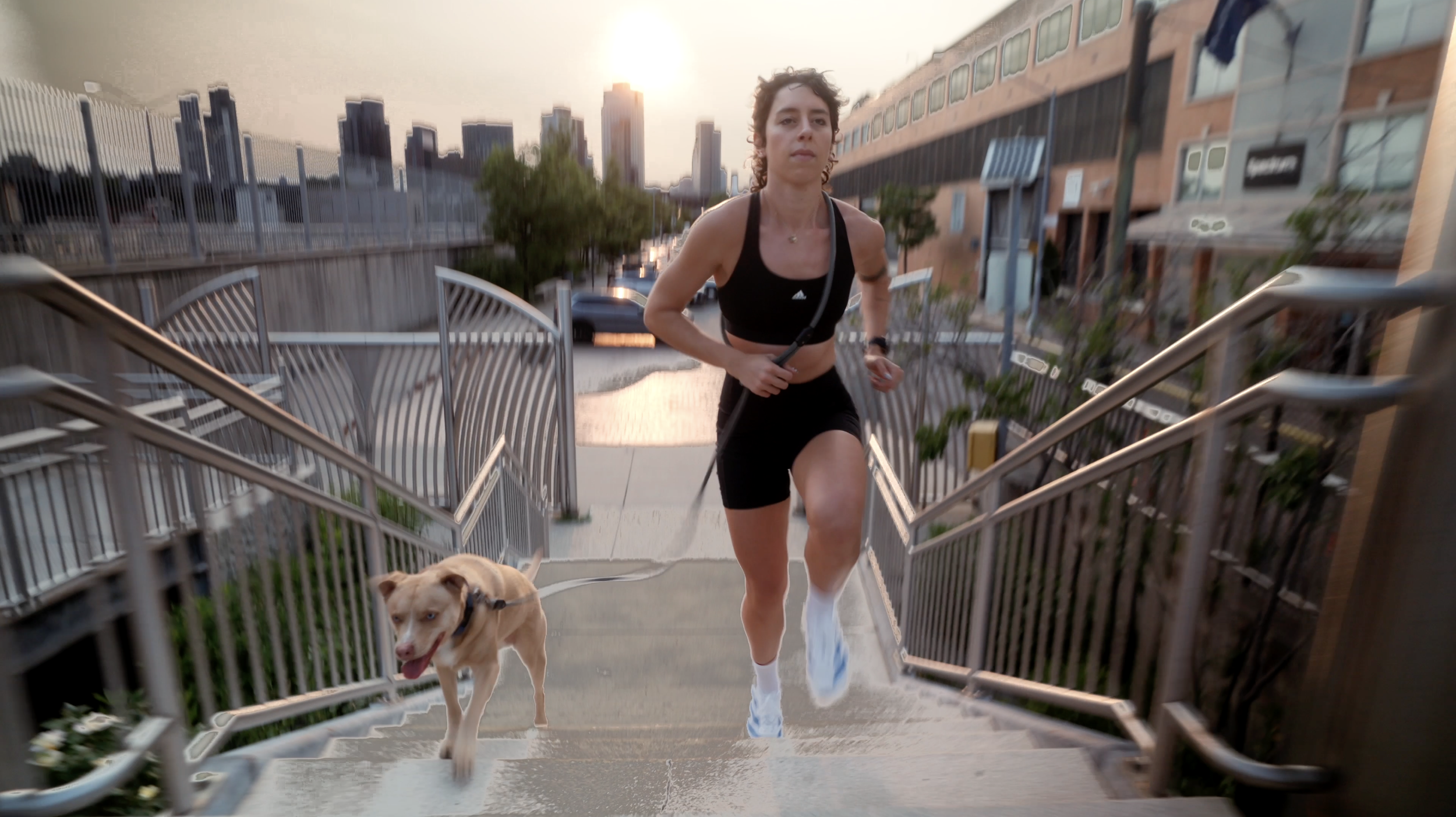 A woman running up outdoor stairs with her dog on a leash during sunset in an urban area.