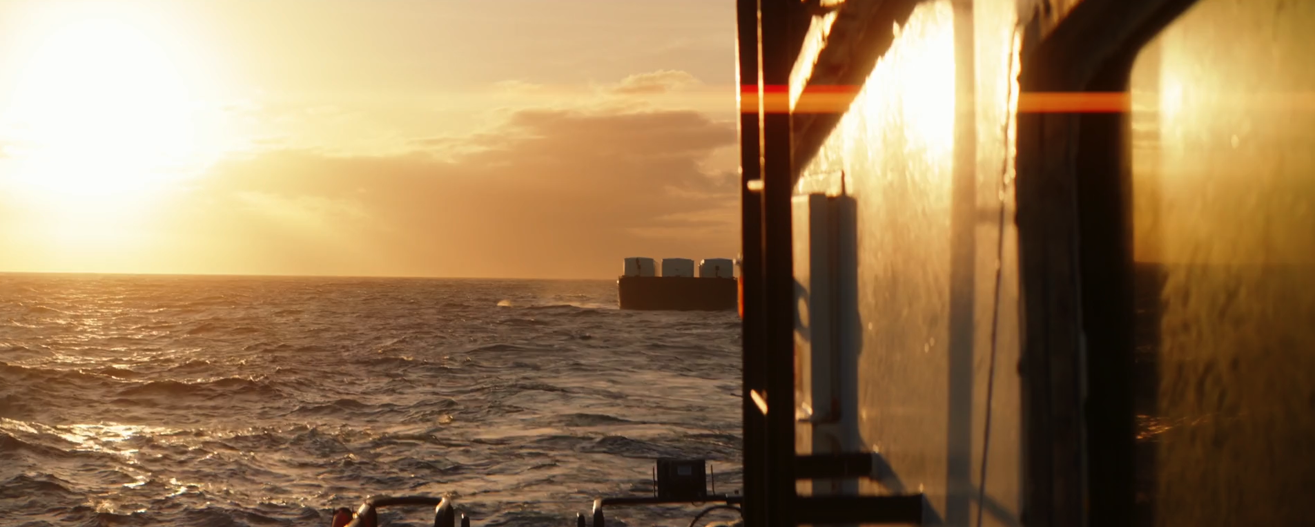 Sunset over the ocean seen from a ship's deck with part of the ship's surface and equipment visible in the foreground.