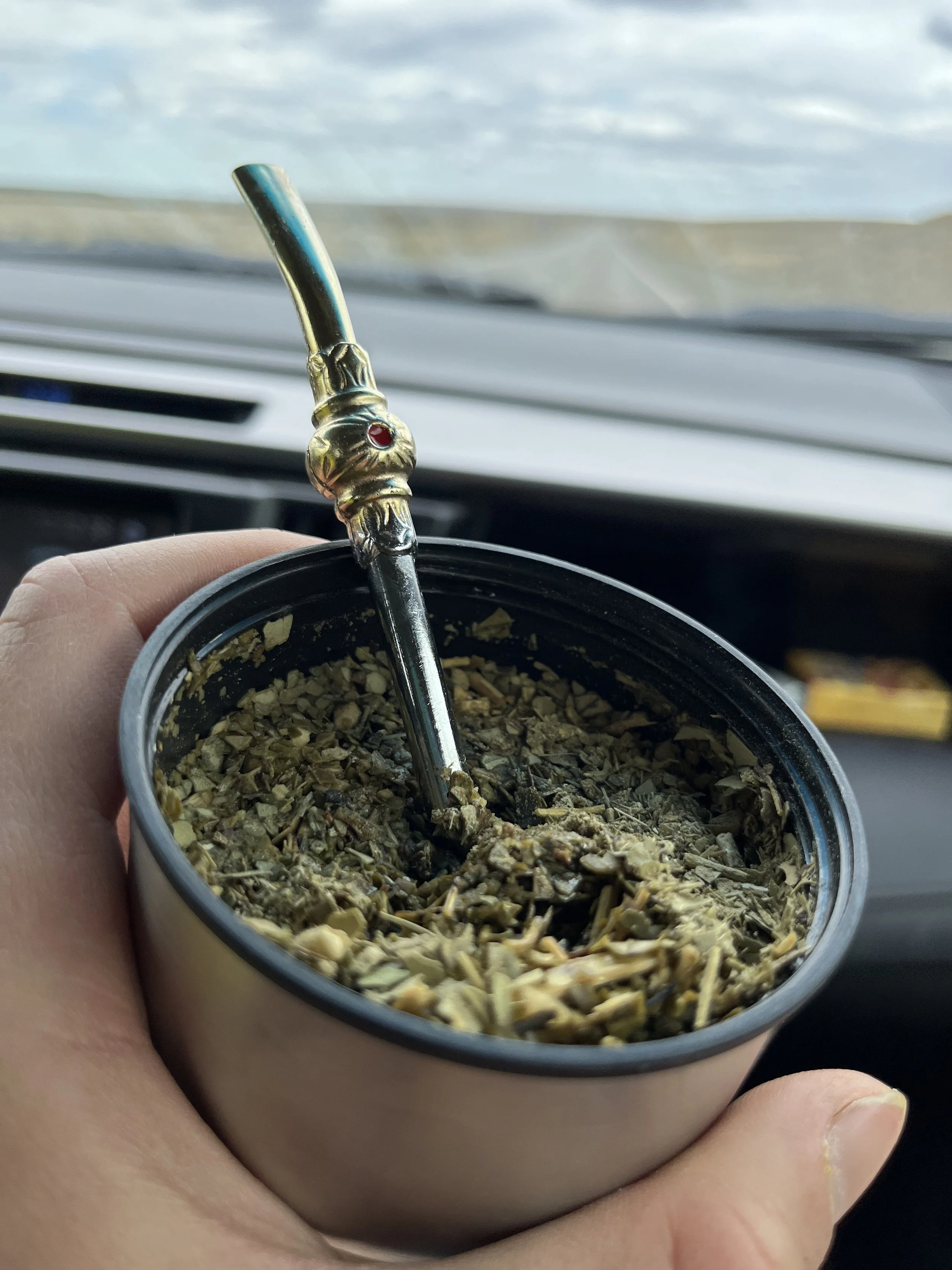Close-up of a hand holding a tin of loose tobacco with a metal pipe in the tin.