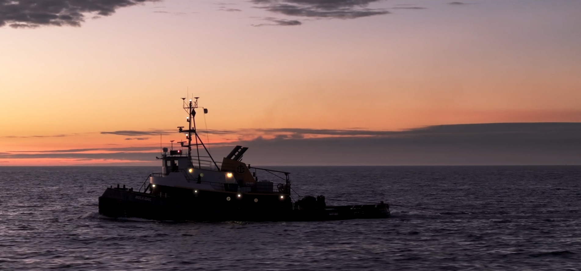 A boat sailing on the ocean at sunset with the sky filled with orange and purple hues.
