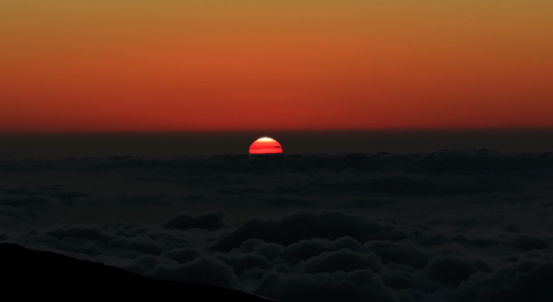 Sunset view over clouds with a partly visible sun on the horizon