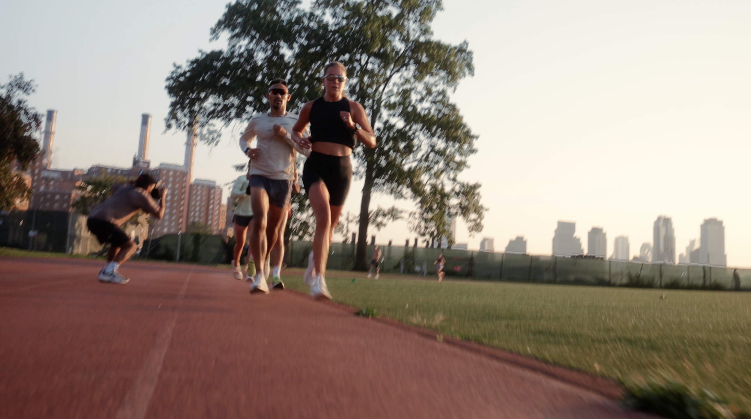 People running on a track at sunset with city skyline in the background.