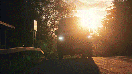A car driving on a road with sunlight shining directly behind it, creating a silhouette effect.