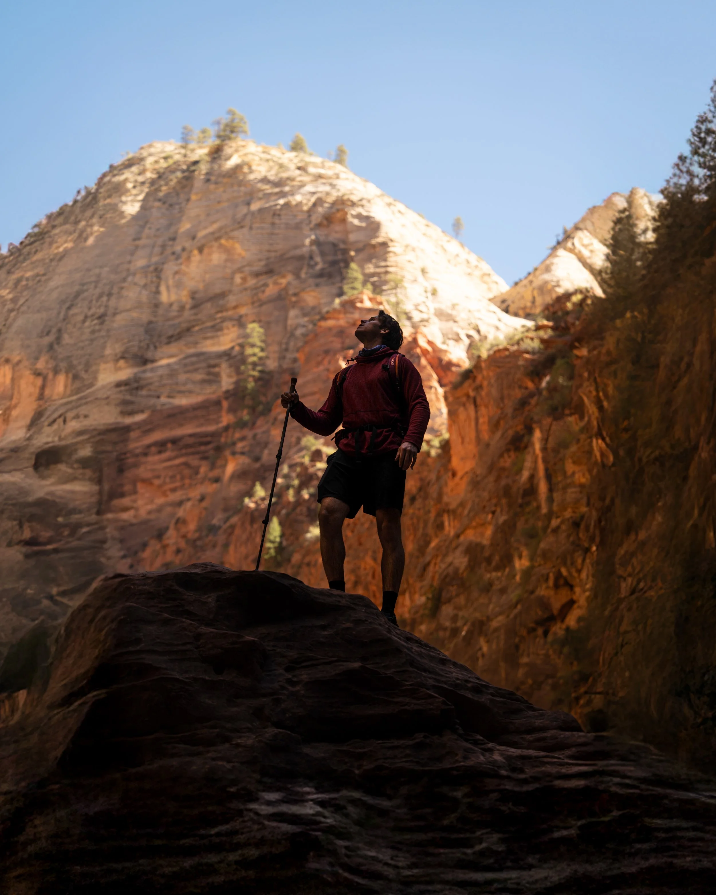 A man hiking on a large rock with a mountain and clear blue sky in the background.