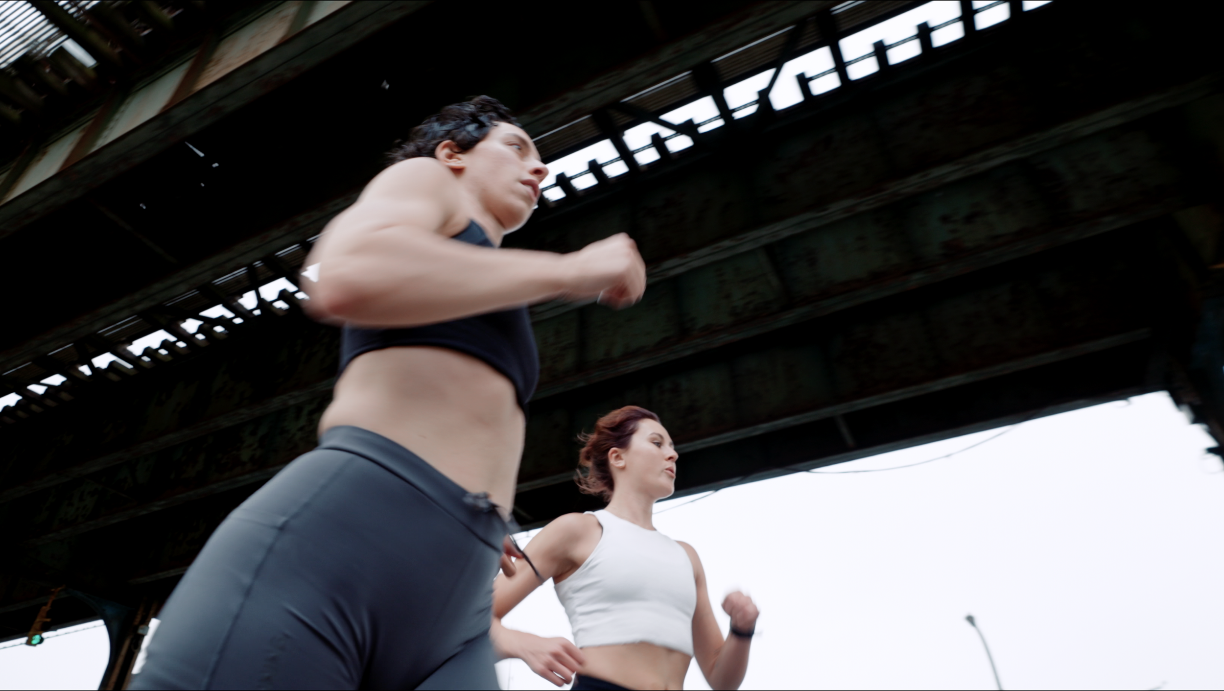 Two women jogging under a bridge during daytime.