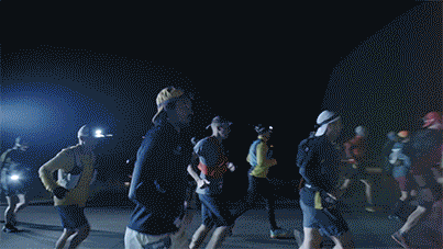 Group of people running at night in an outdoor setting with bright artificial lights.