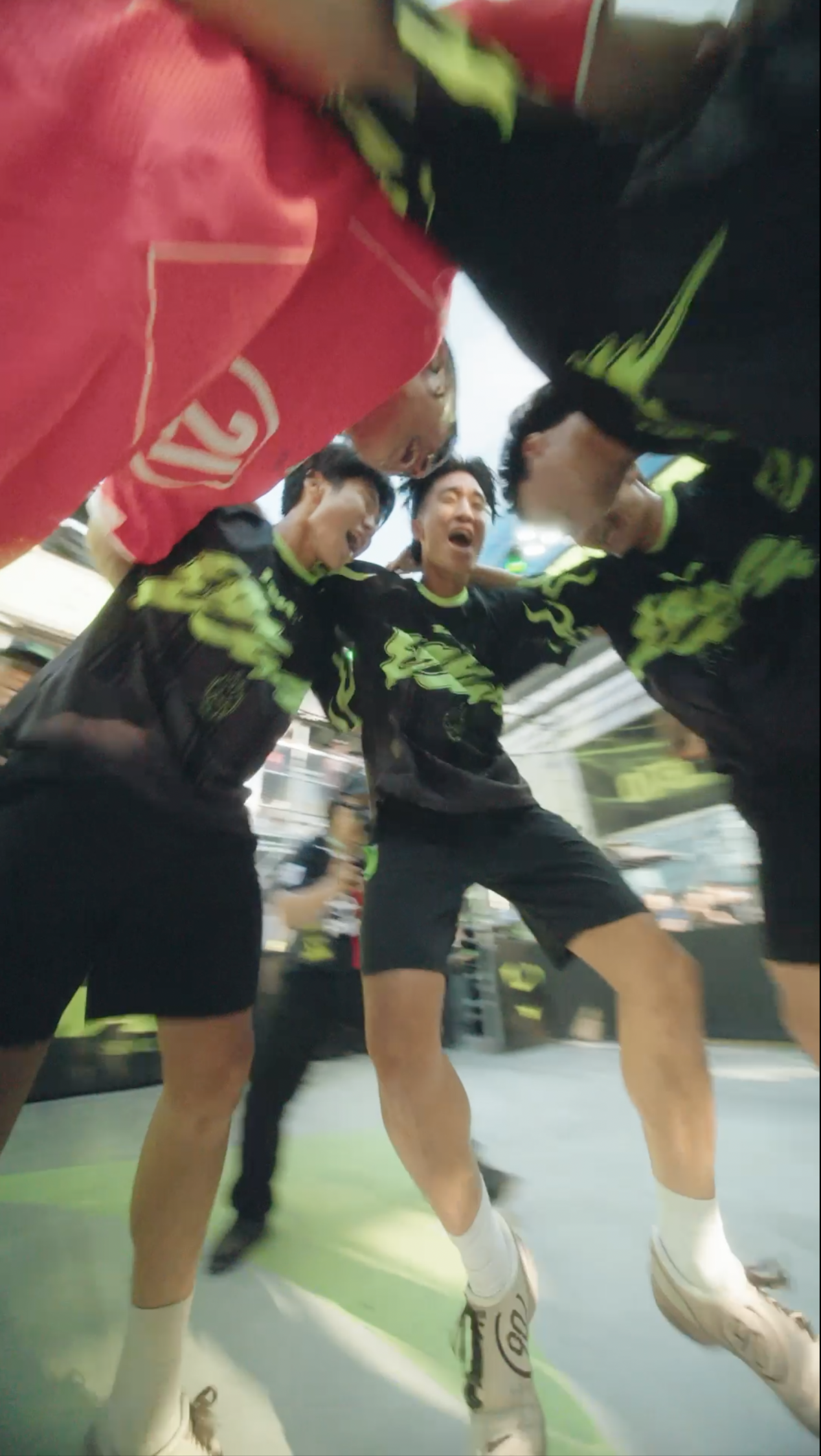 A group of young male athletes in black and neon green uniforms huddle together and celebrate during an indoor sports event.